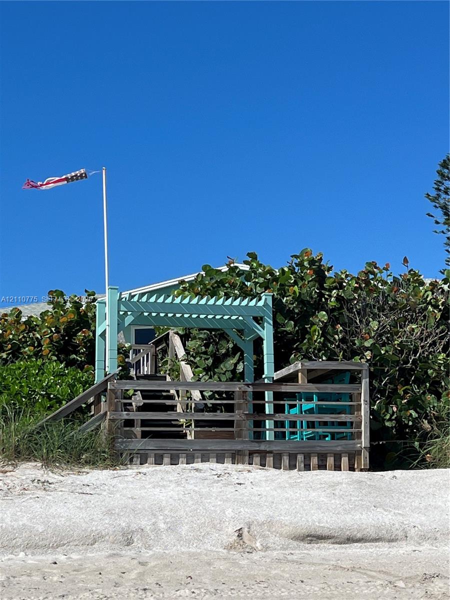 Coastal wood deck featuring a painted pergola, stair access, and integrated railing