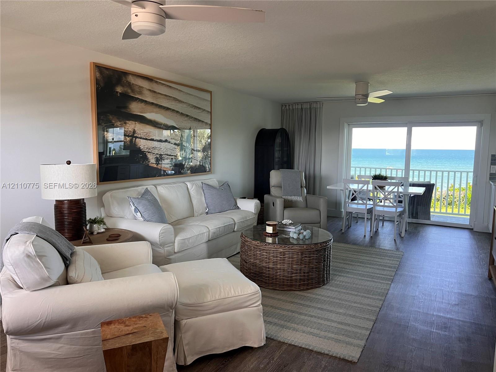 Living area featuring wood-finish flooring, white ceiling fans, and sliding glass doors with direct access to an exterior balcony Living area featuring wood-finish flooring, white ceiling fans, and sliding glass doors with direct access to an exterior balcony