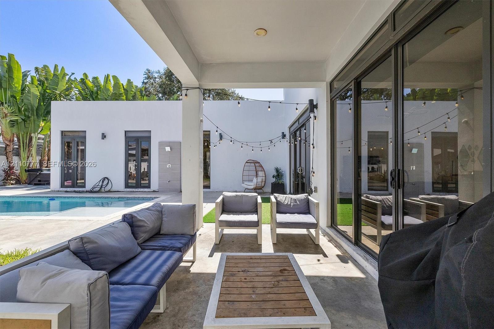 Covered patio featuring concrete flooring, sliding glass door systems, recessed ceiling lighting, and overhead string lights, situated near a swimming pool