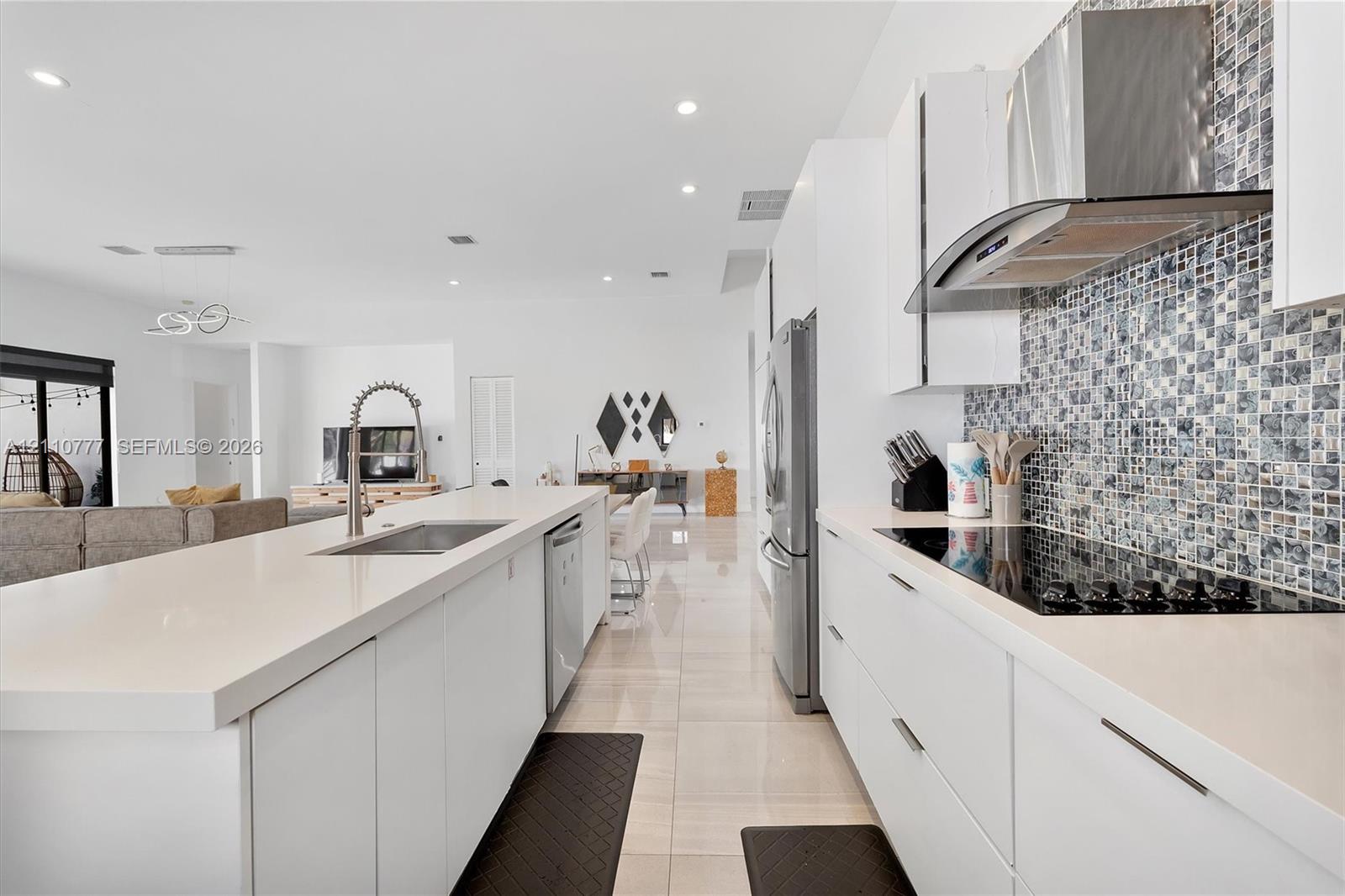 Kitchen featuring flat-panel white cabinetry, quartz countertops, a mosaic tile backsplash, a stainless steel range hood, and large-format tile flooring Kitchen featuring flat-panel white cabinetry, quartz countertops, a mosaic tile backsplash, a stainless steel range hood, and large-format tile flooring