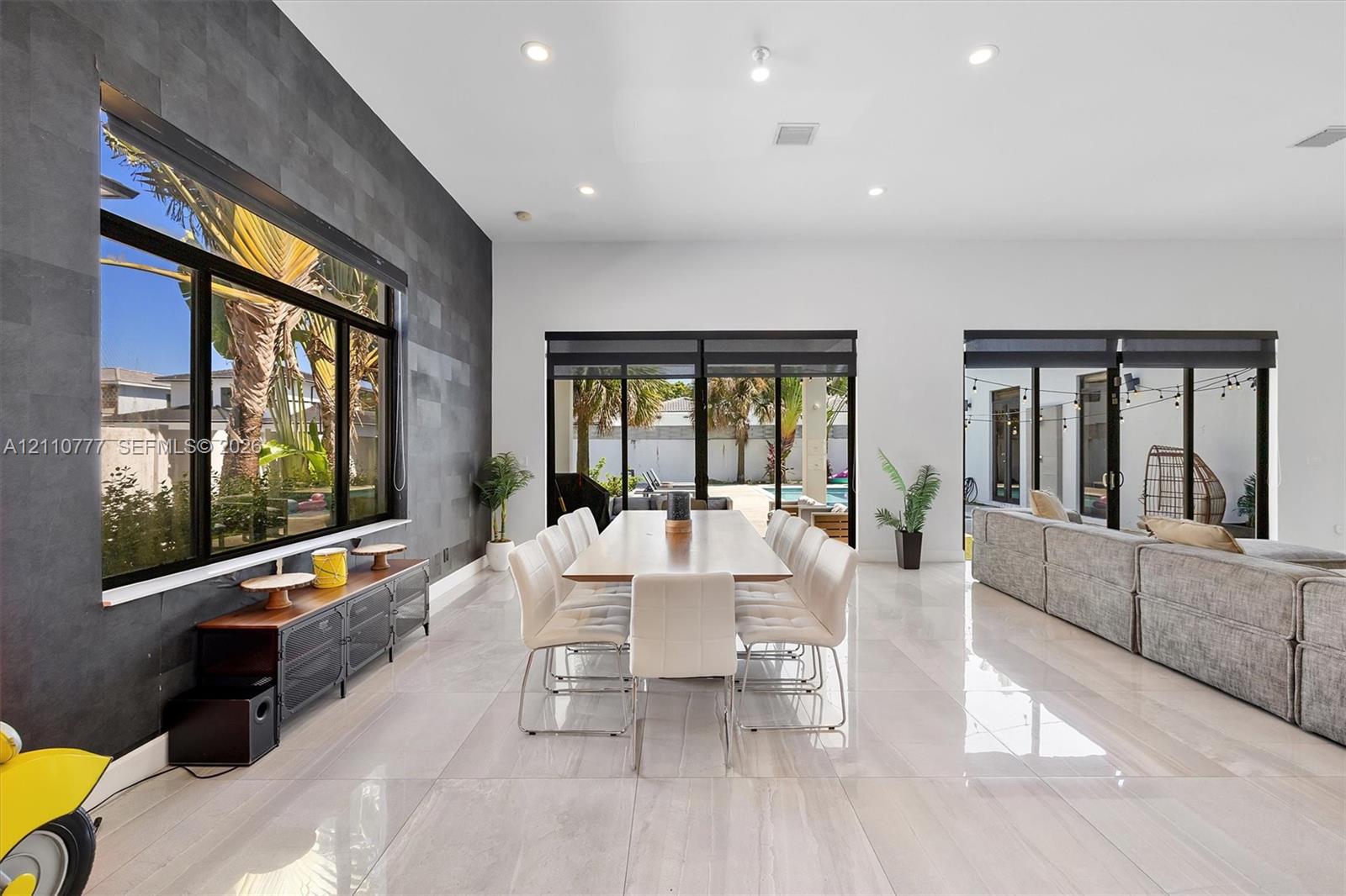 Spacious interior featuring large-format tile flooring, a charcoal-toned textured accent wall, recessed lighting, and multiple sliding glass door systems Spacious interior featuring large-format tile flooring, a charcoal-toned textured accent wall, recessed lighting, and multiple sliding glass door systems