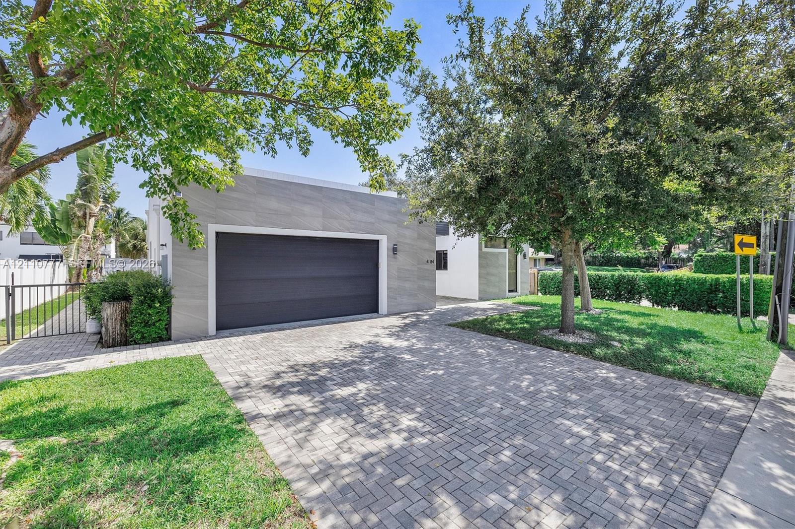 Detached garage with large-format stone-textured exterior cladding, paved brick driveway, metal gate, and manicured landscaping Detached garage with large-format stone-textured exterior cladding, paved brick driveway, metal gate, and manicured landscaping