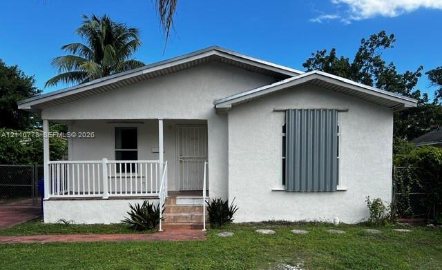 Stucco exterior featuring a covered front porch, white railing, metal storm shutter, and a front-facing gable roof