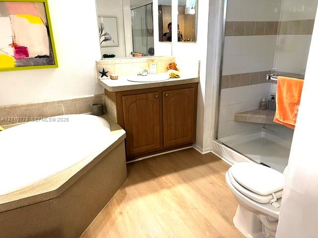 Bathroom featuring wood-finish flooring, a separate soaking tub with a tiled surround, a built-in vanity with an inset sink, and a glass-enclosed shower with a tiled bench seat