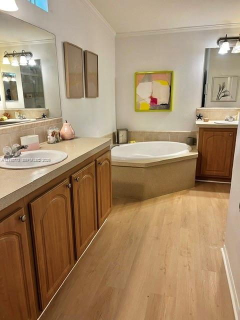 Dual vanity featuring stone-finish countertops with drop-in sinks, wood-finish cabinetry, an oval soaking tub with a tiled surround, and wood-finish flooring