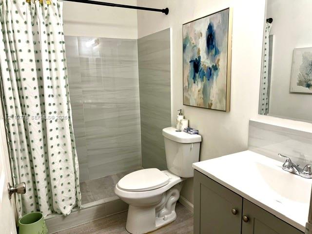 Bathroom featuring neutral-toned tile shower surround, grey vanity cabinet with integrated white countertop, and brushed metallic hardware