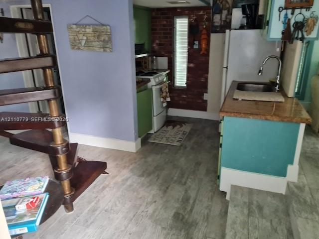 Spiral wooden staircase with turned spindles, exposed brick accent wall, wood-finish flooring, and kitchen island featuring a stainless steel undermount sink with a gooseneck faucet