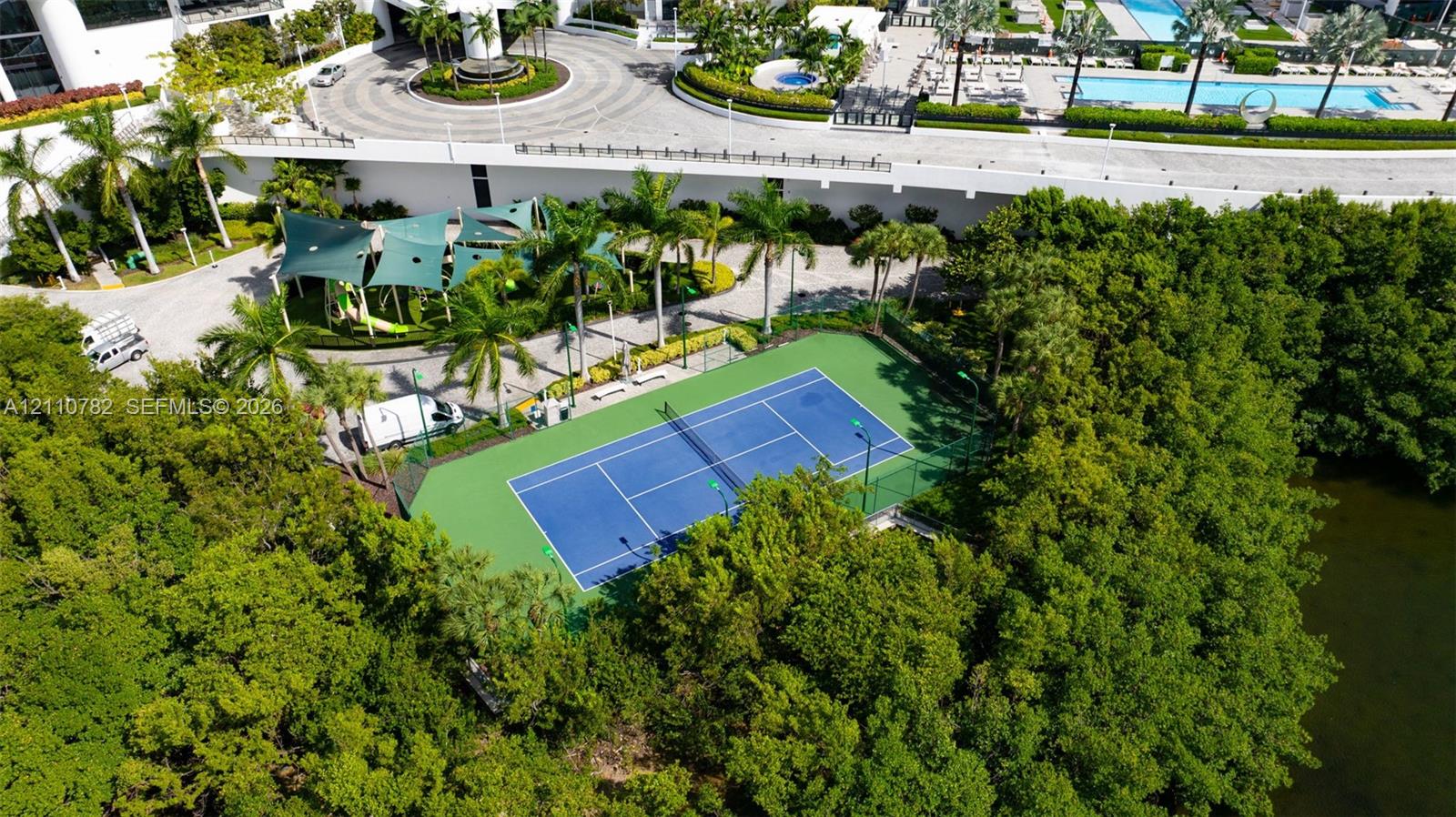 Tennis court with perimeter fencing, outdoor swimming pool, circular paved motor court, and canopy-covered recreation area
