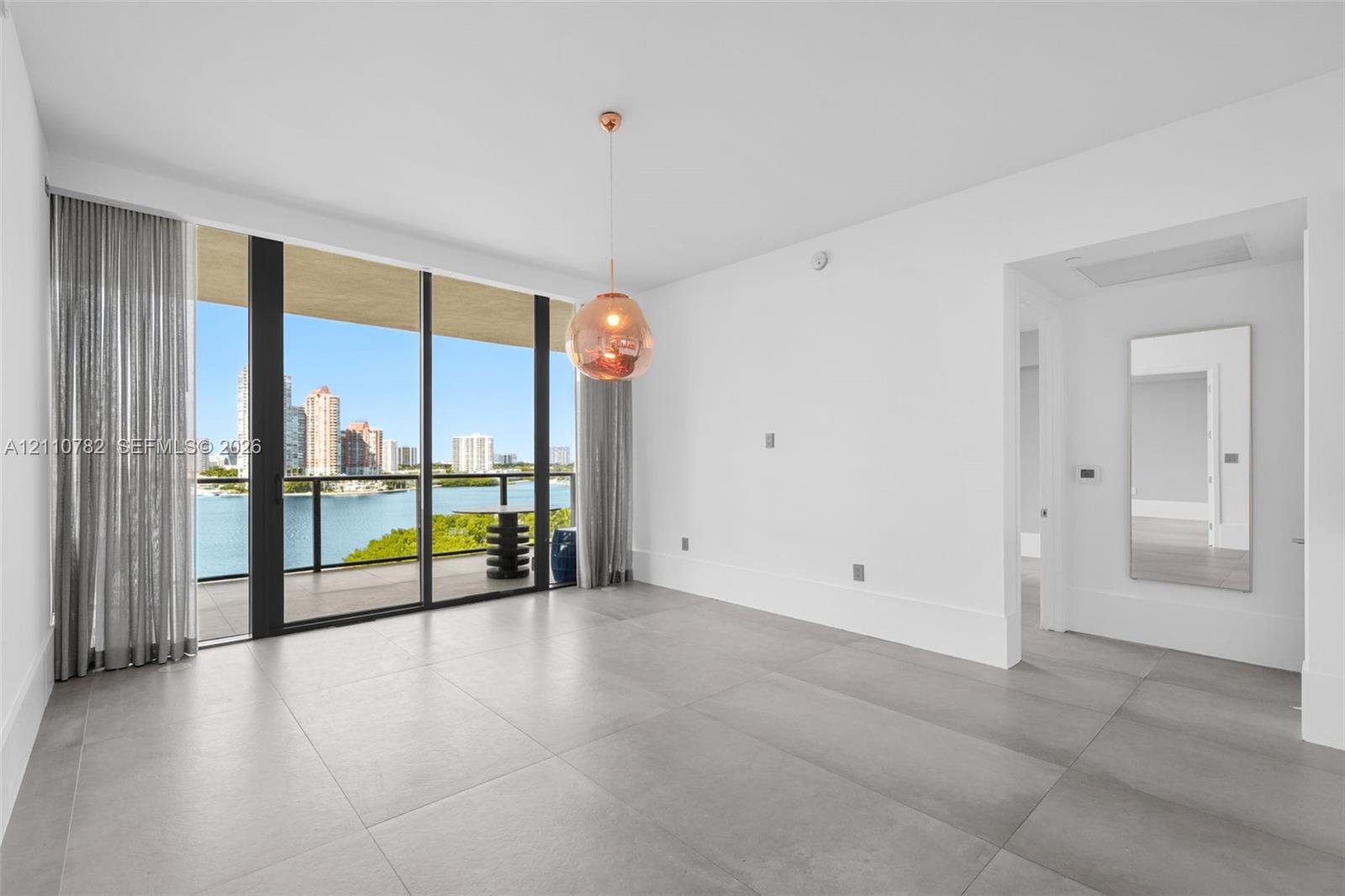 Floor-to-ceiling sliding glass doors, private balcony, large-format tile flooring, metallic pendant lighting, and wall-mounted mirror
