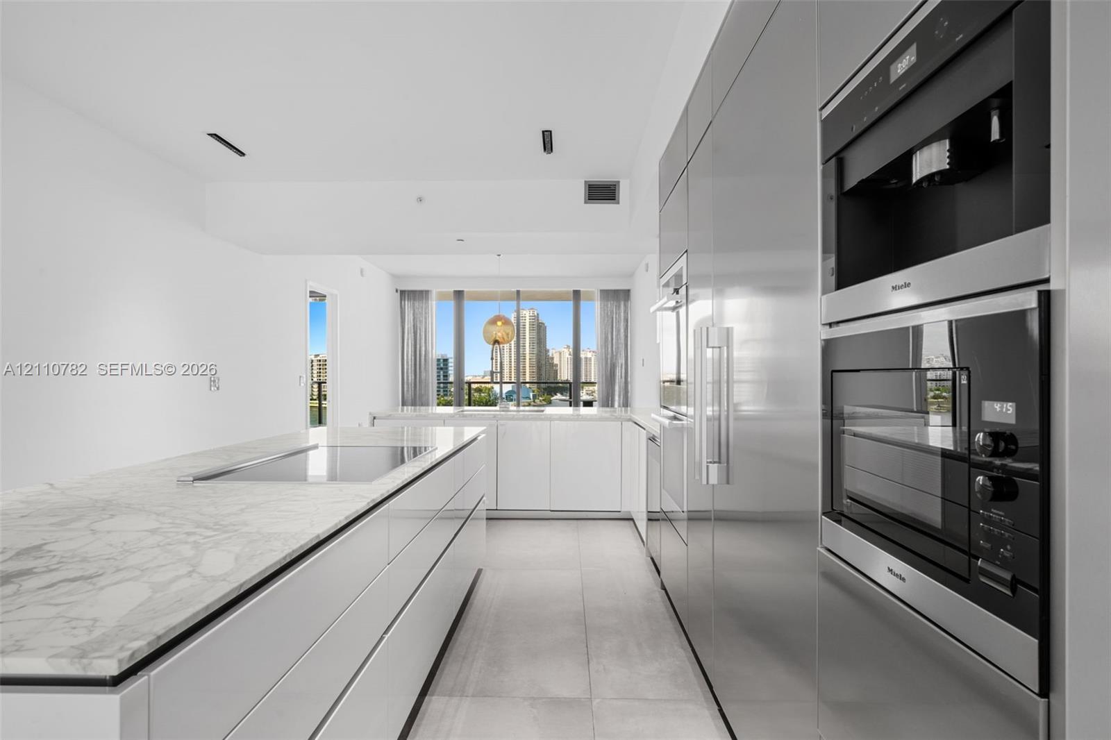 Contemporary kitchen featuring a stone-surface island with an integrated cooktop, flat-panel cabinetry, high-end built-in stainless steel appliances, and large-format floor tiling