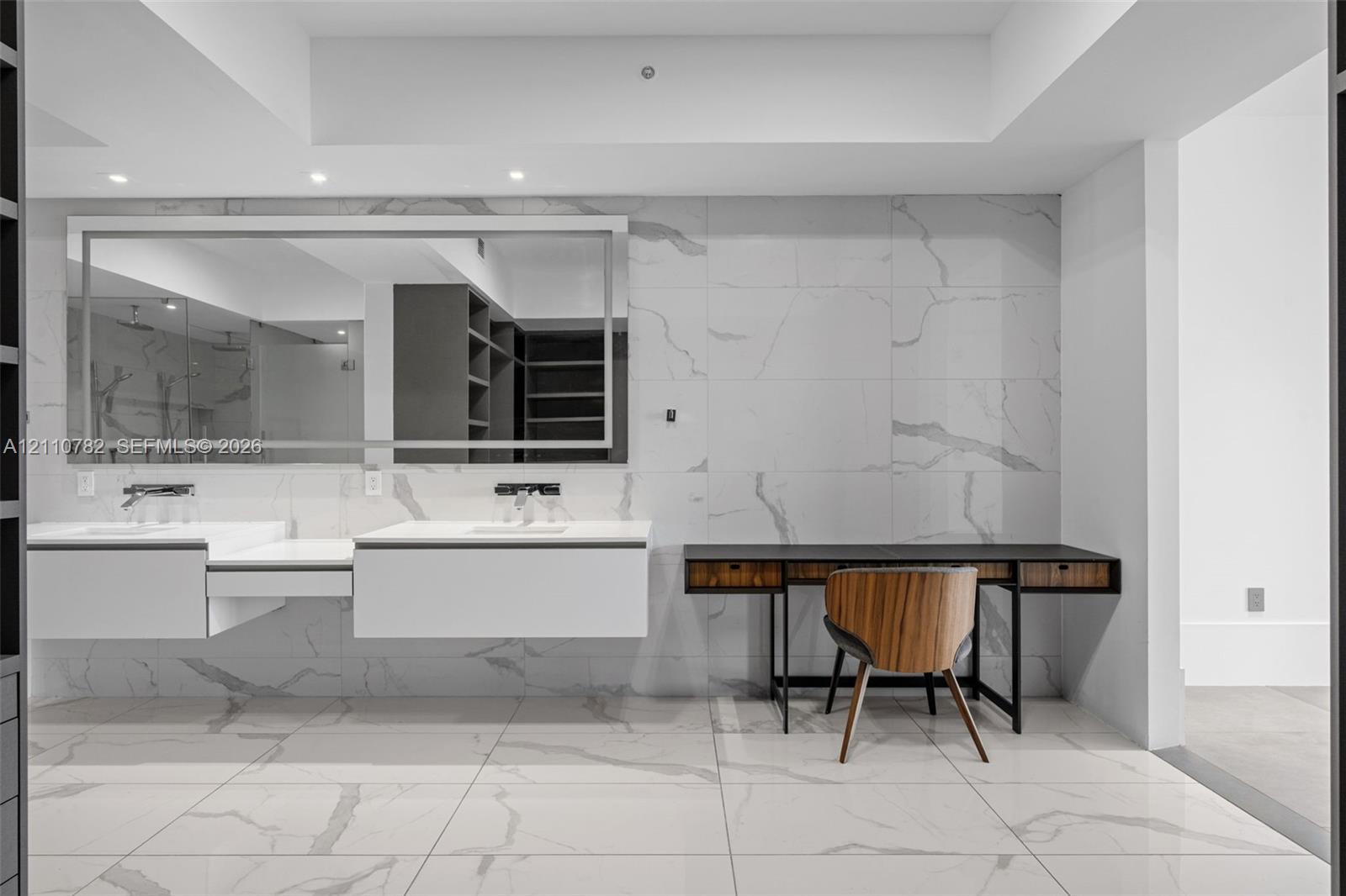 Floating dual vanity with integrated sinks, large-format stone-finish tile flooring and wall cladding, recessed lighting, and expansive wall-to-wall vanity mirror