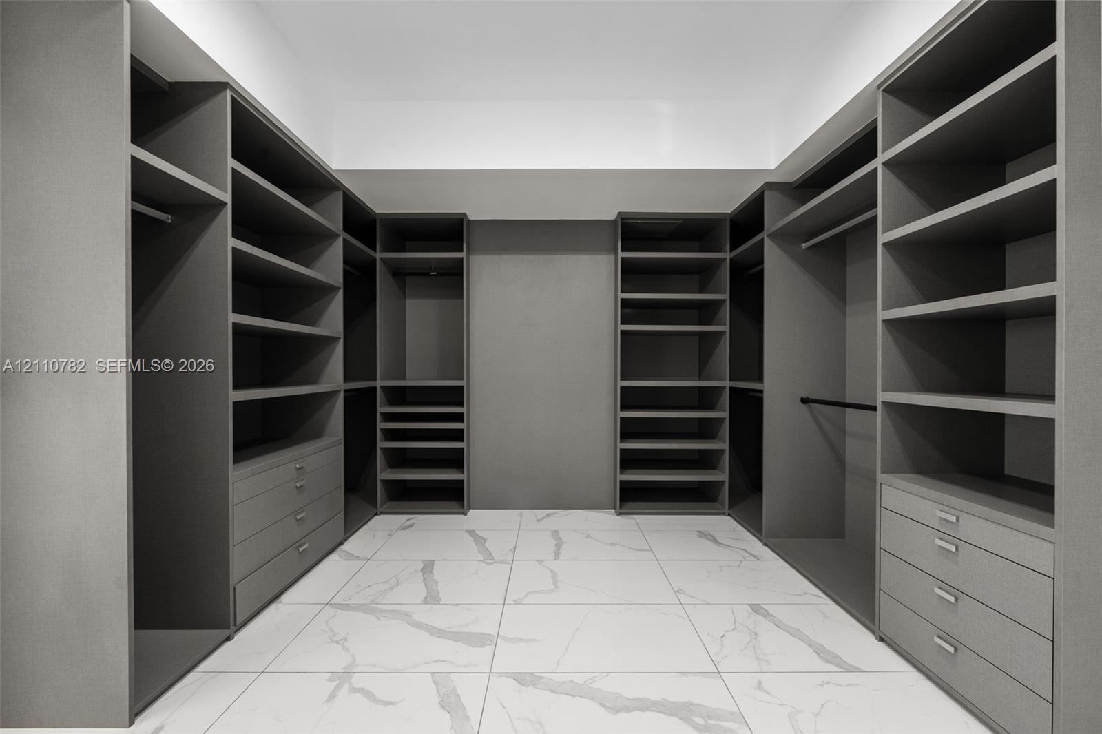 Walk-in closet featuring extensive built-in shelving, integrated hanging rods, custom cabinetry with pull-out drawers, and large-format tile flooring