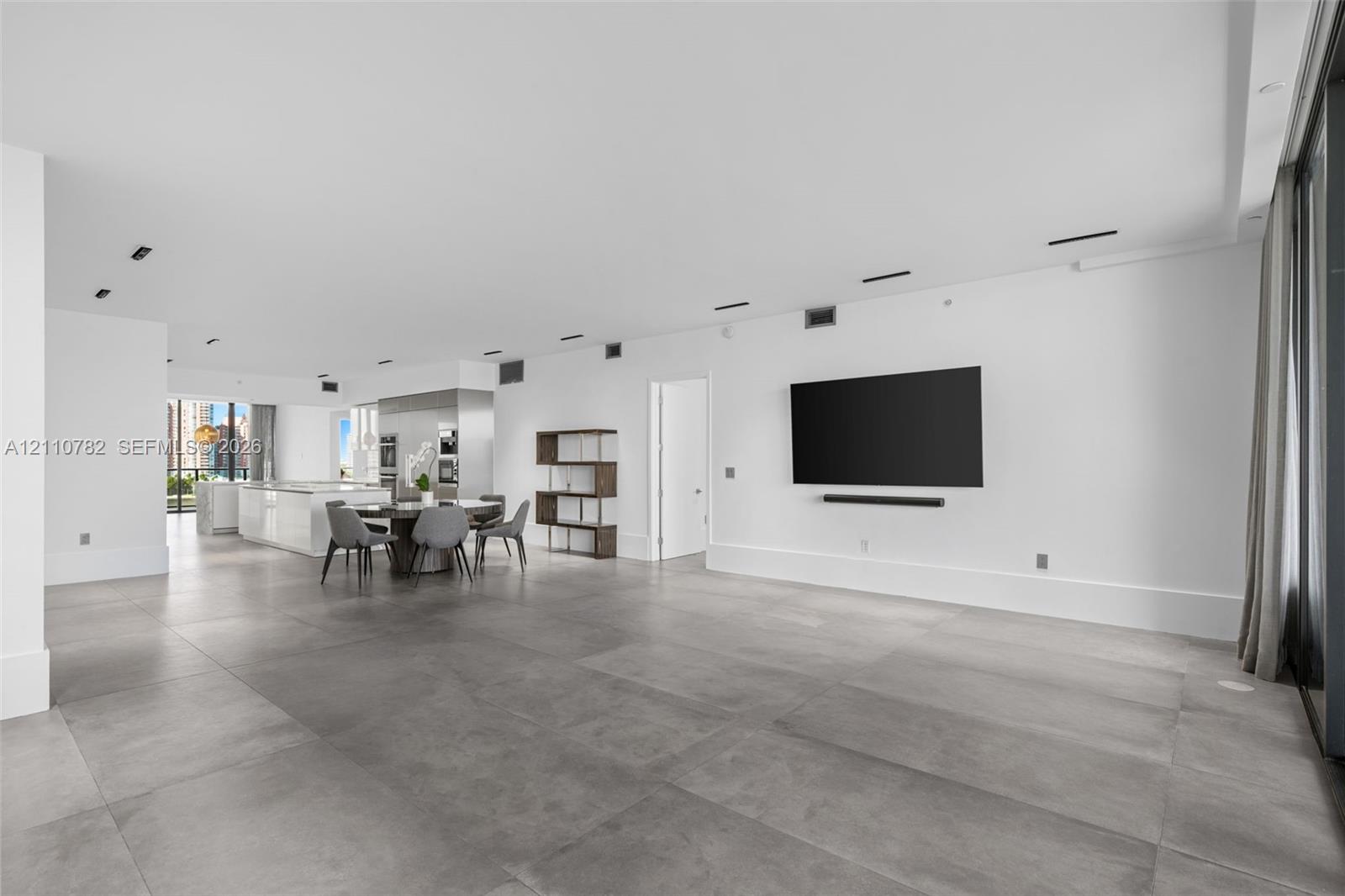 Open concept interior featuring large-format grey tile flooring, recessed ceiling lighting, and a neutral white color palette