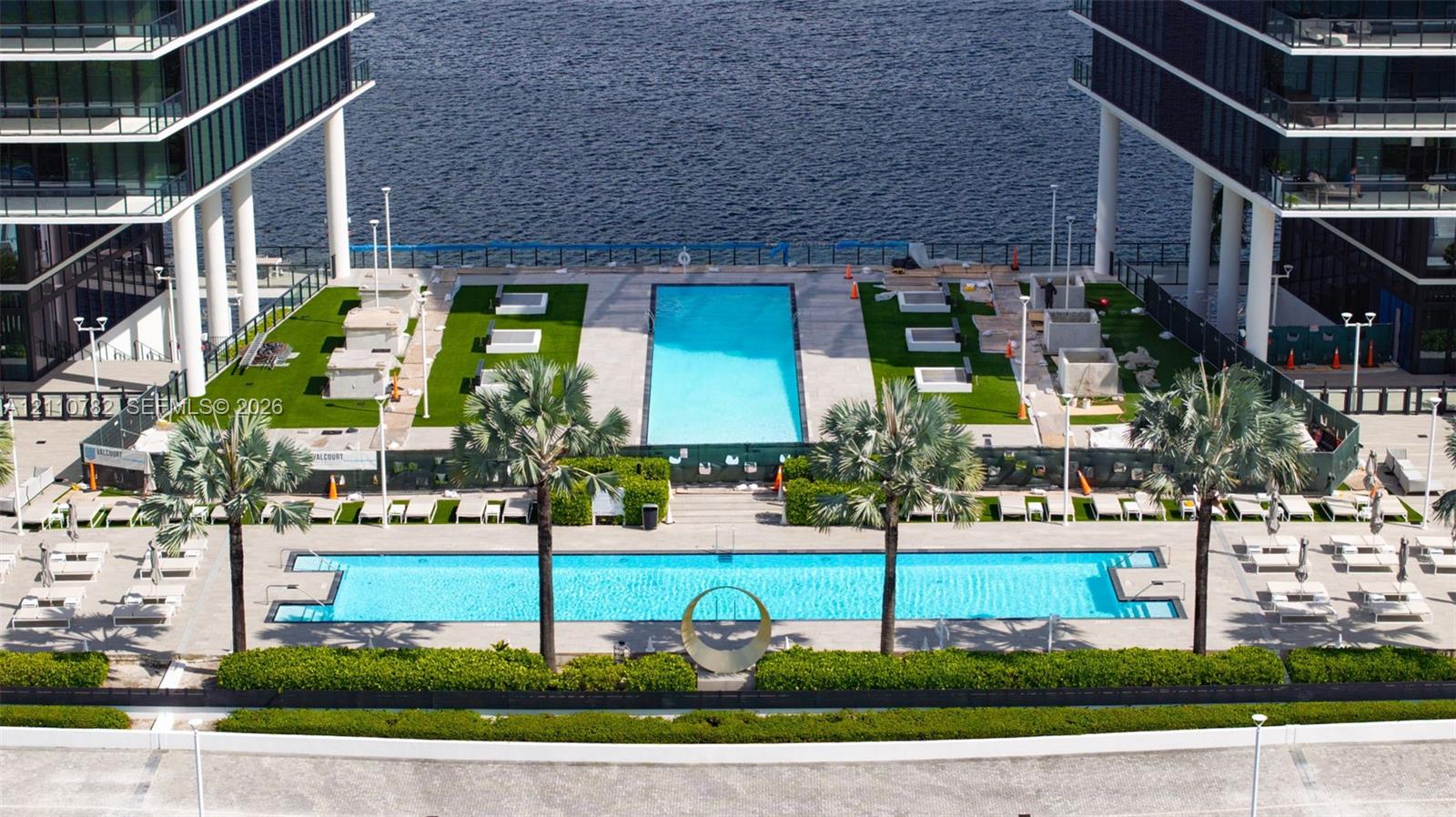 Outdoor terrace featuring two rectangular swimming pools, synthetic turf areas, paved stone decking, and manicured hedges