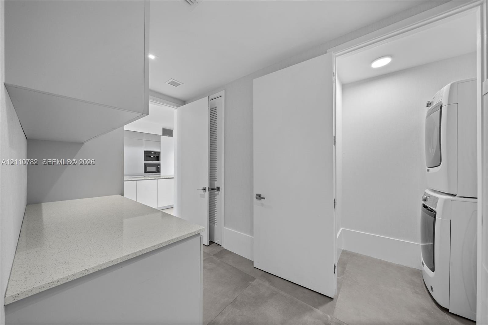 Utility area featuring stone-surface countertop, built-in cabinetry, large-format tile flooring, and dedicated laundry closet with stacked appliance configuration