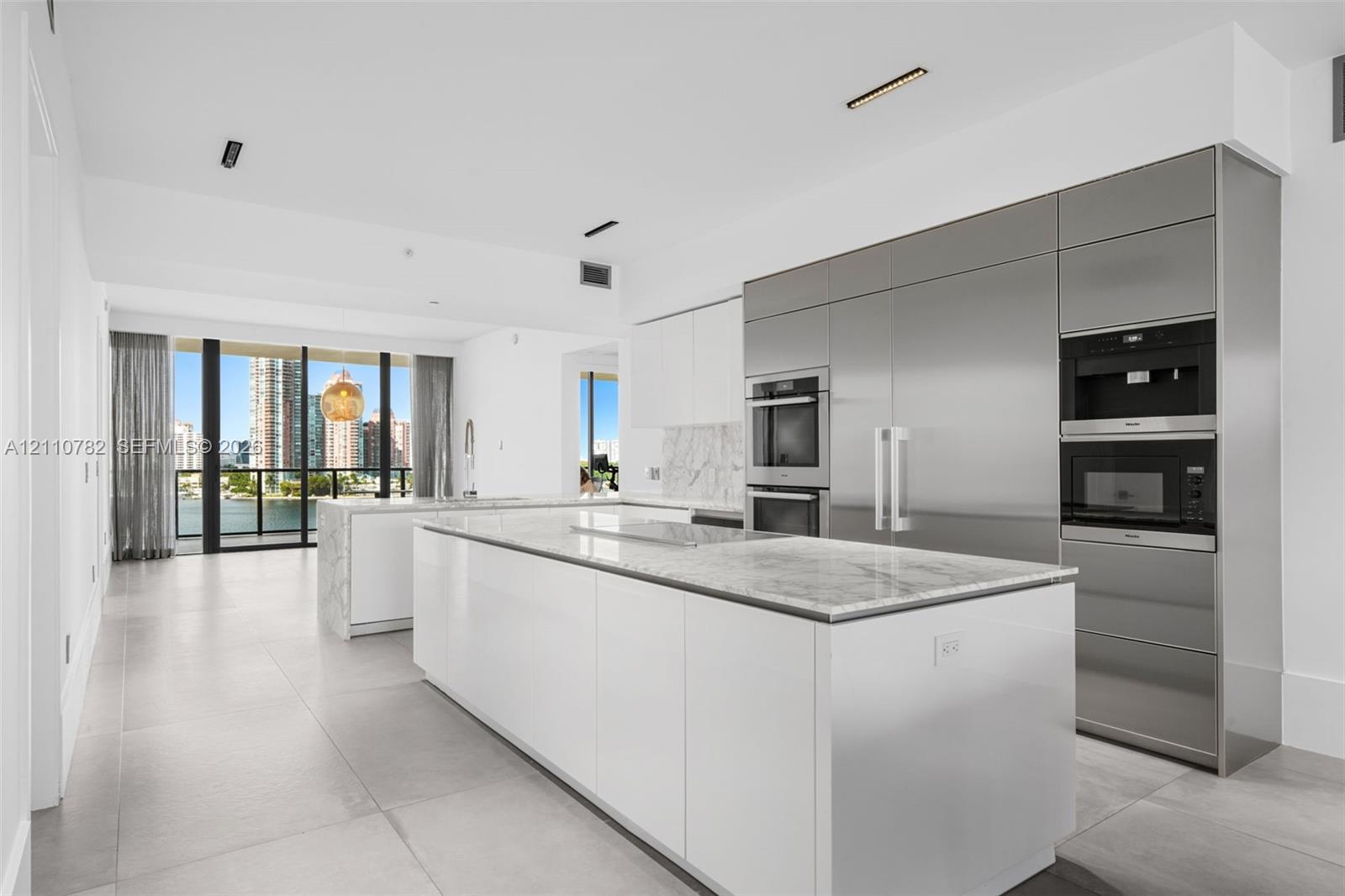 Contemporary kitchen featuring dual islands with stone-surface countertops, floor-to-ceiling cabinetry, integrated stainless steel appliances, and large-format porcelain tile flooring