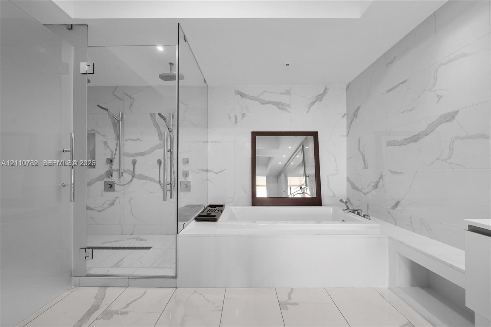 Large-format white tile with grey veining, glass-enclosed walk-in shower with rainfall showerhead, and a deep-soaking drop-in bathtub
