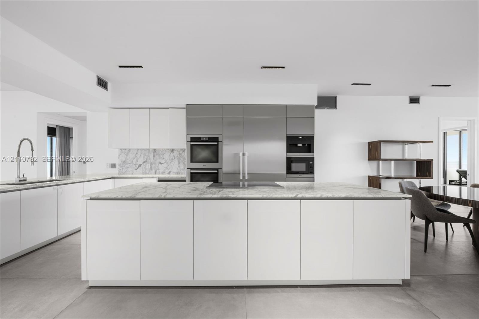 Contemporary kitchen featuring an expansive center island with stone surfacing, stainless steel built-in appliances, flat-panel cabinetry, a stone backsplash, and large-format floor tiling