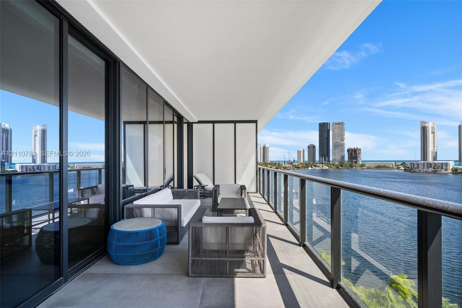 Expansive covered terrace featuring floor-to-ceiling glass panel doors, concrete-finish flooring, and a sleek glass-paneled railing with black framing