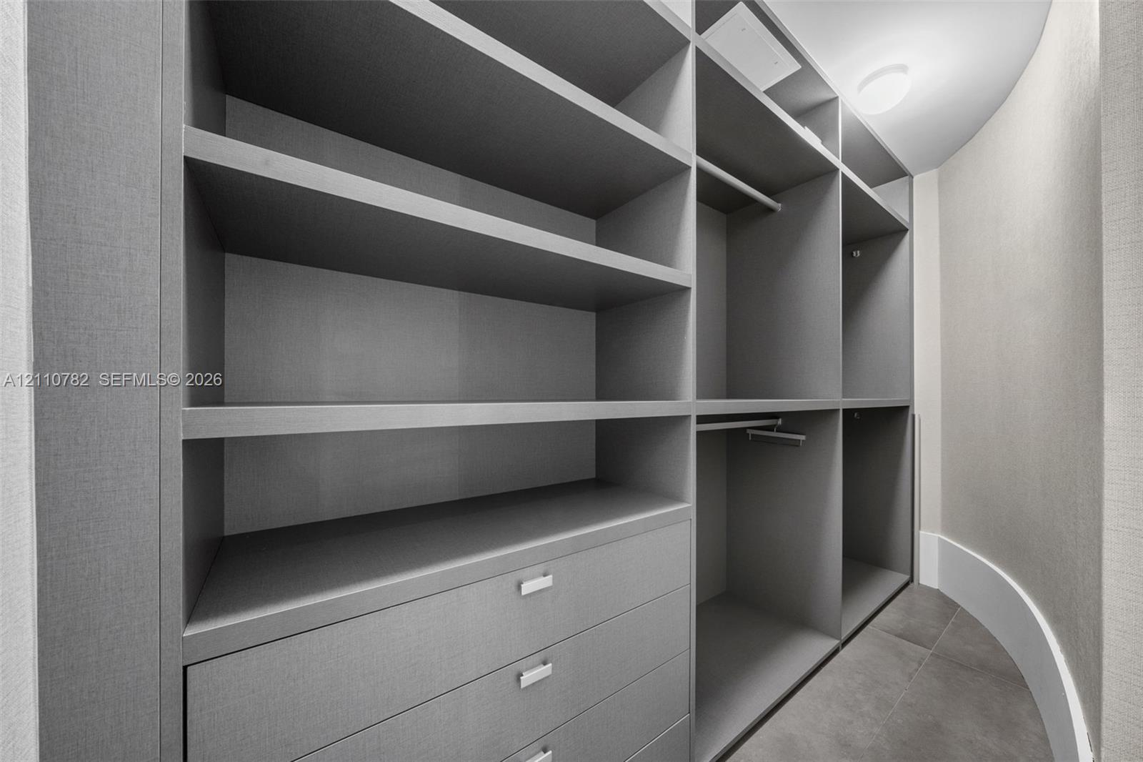 Custom organizational system featuring floor-to-ceiling cabinetry, integrated shelving, hanging rods, and built-in drawers with metallic hardware, set against tiled flooring