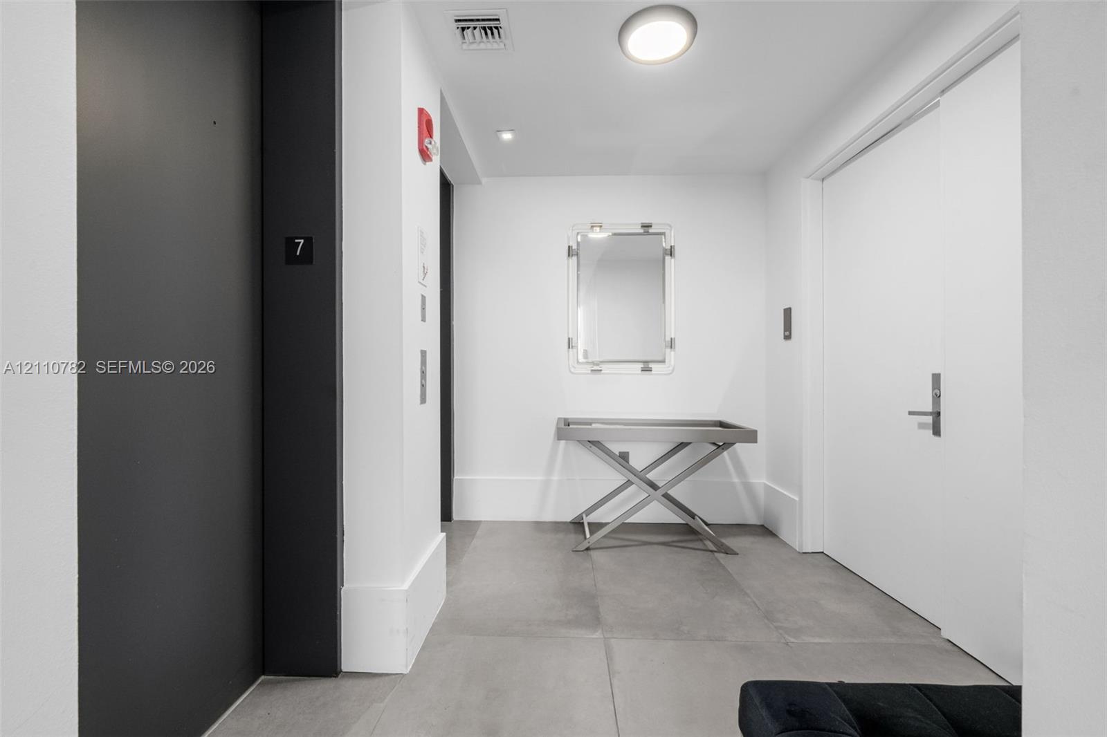 Entry foyer featuring large-format grey tile flooring, minimalist white walls, recessed ceiling lighting, and a matte black elevator entrance Entry foyer featuring large-format grey tile flooring, minimalist white walls, recessed ceiling lighting, and a matte black elevator entrance