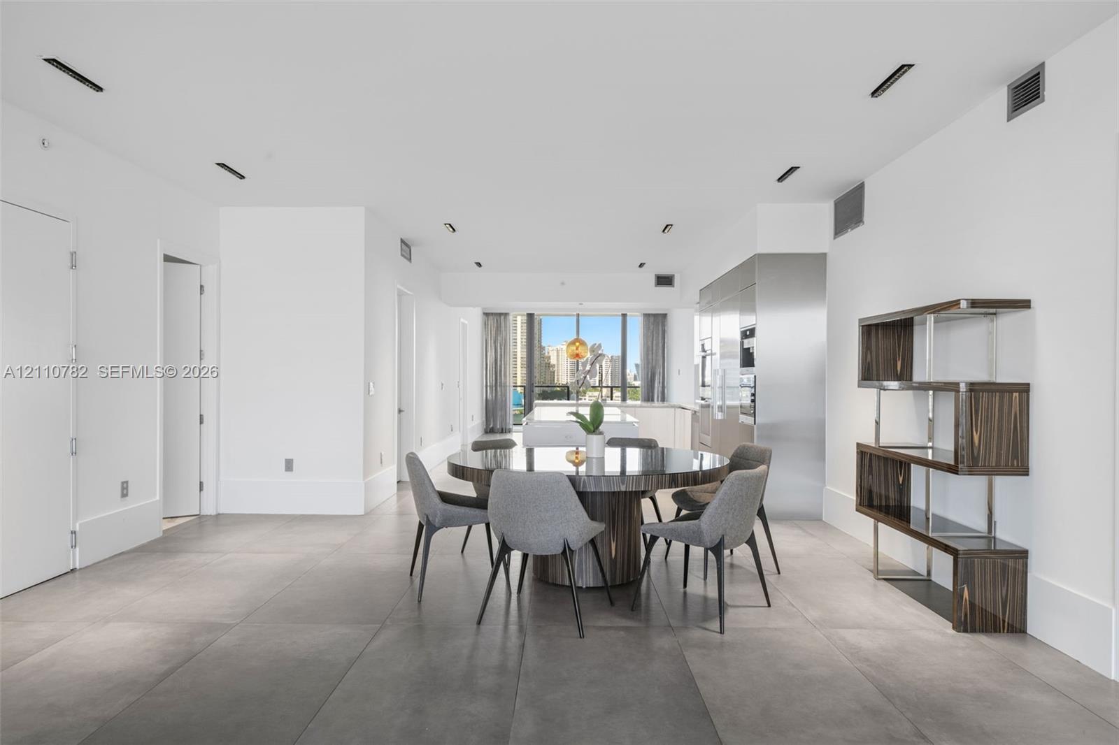 Open-concept space featuring large-format ceramic tile flooring, floor-to-ceiling windows, integrated stainless steel kitchen cabinetry, and recessed ceiling lighting