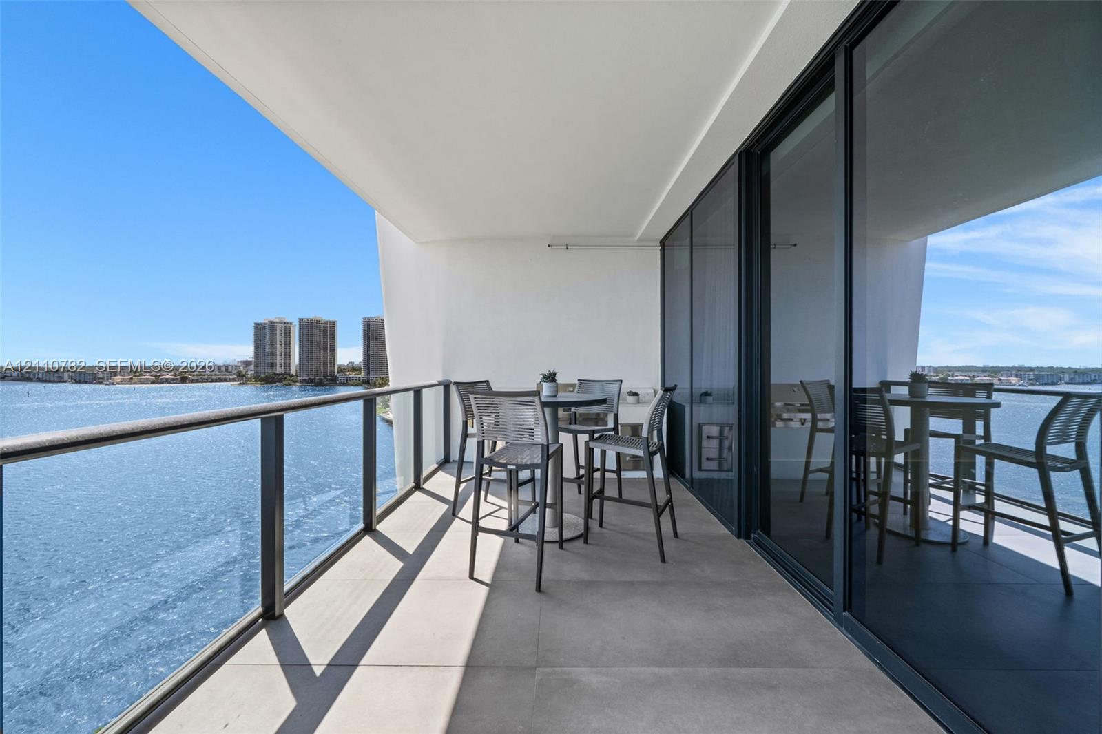 Covered balcony featuring large-format stone tile flooring, a metal and glass railing system, and full-height sliding glass doors