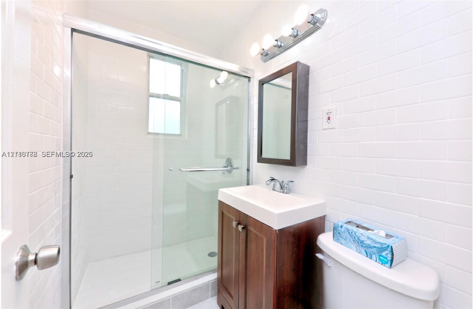 Bathroom featuring a glass-enclosed shower with subway tile surround, wood-finish vanity, rectangular wall-mounted medicine cabinet, and four-bulb vanity lighting