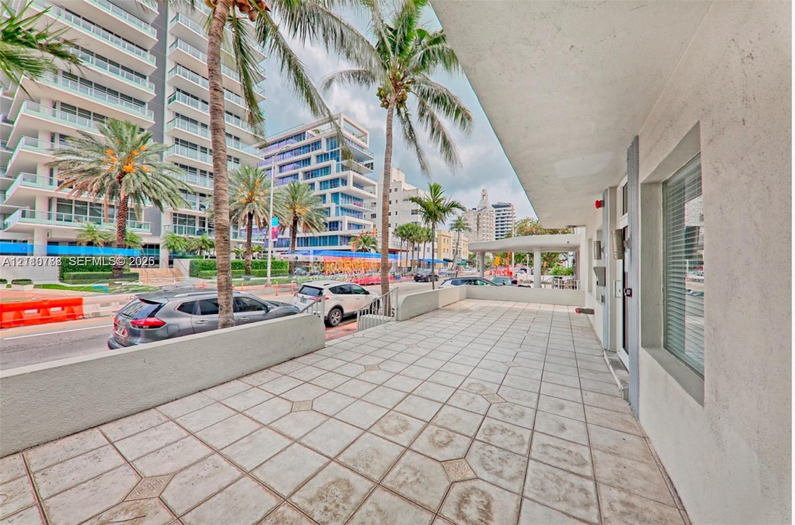 Covered exterior terrace featuring geometric tile flooring, concrete perimeter wall, and built-in glass paneled entry