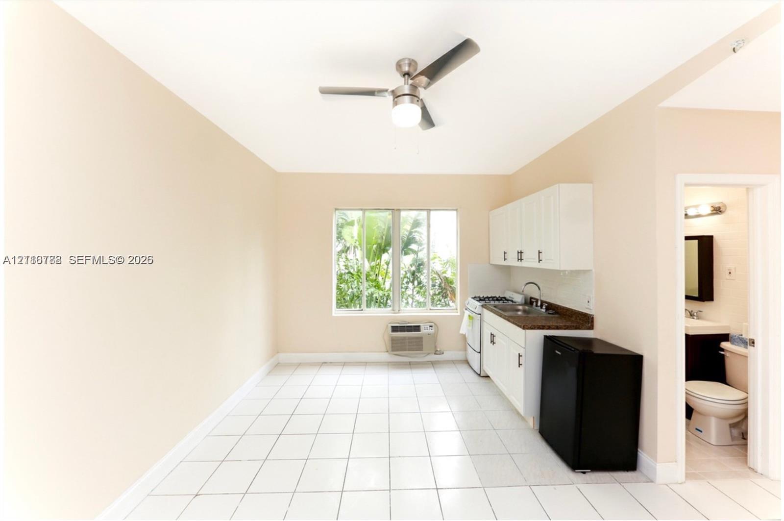 Kitchenette featuring white cabinetry, dark stone-finish countertops, stainless steel sink with pull-down faucet, and white ceramic tile flooring, complemented by a ceiling fan