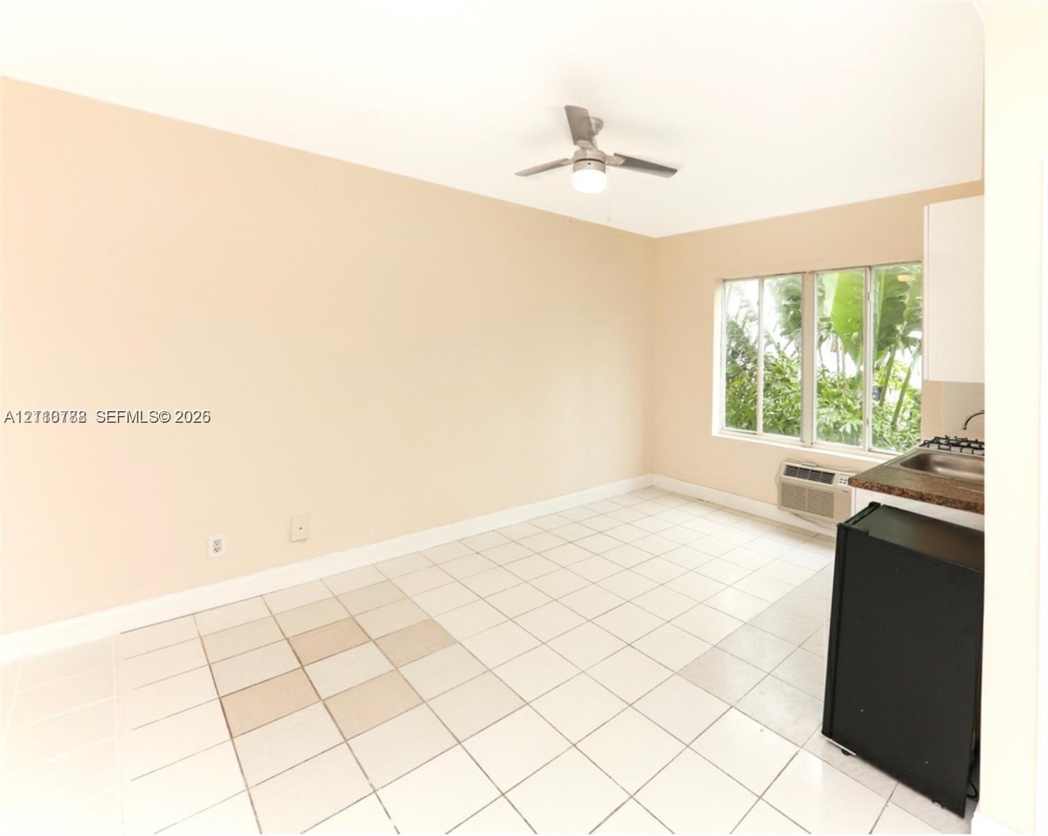 Interior space featuring neutral wall paint, white tile flooring, a ceiling fan with an integrated light fixture, large multi-pane windows, and a built-in kitchenette area with a sink