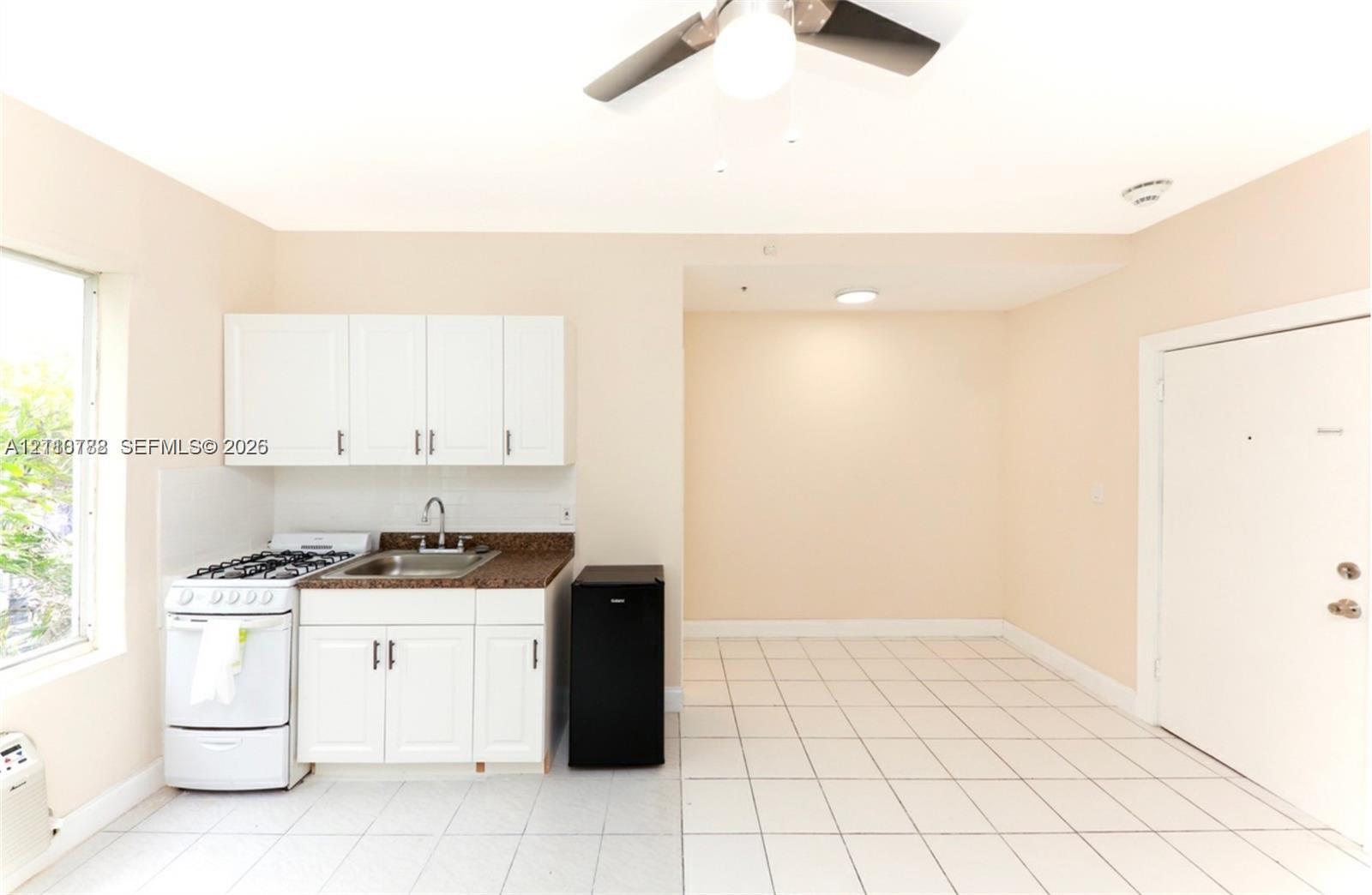 Kitchenette featuring white cabinetry, stone-finish countertops, stainless steel sink with gooseneck faucet, gas range, and tile flooring