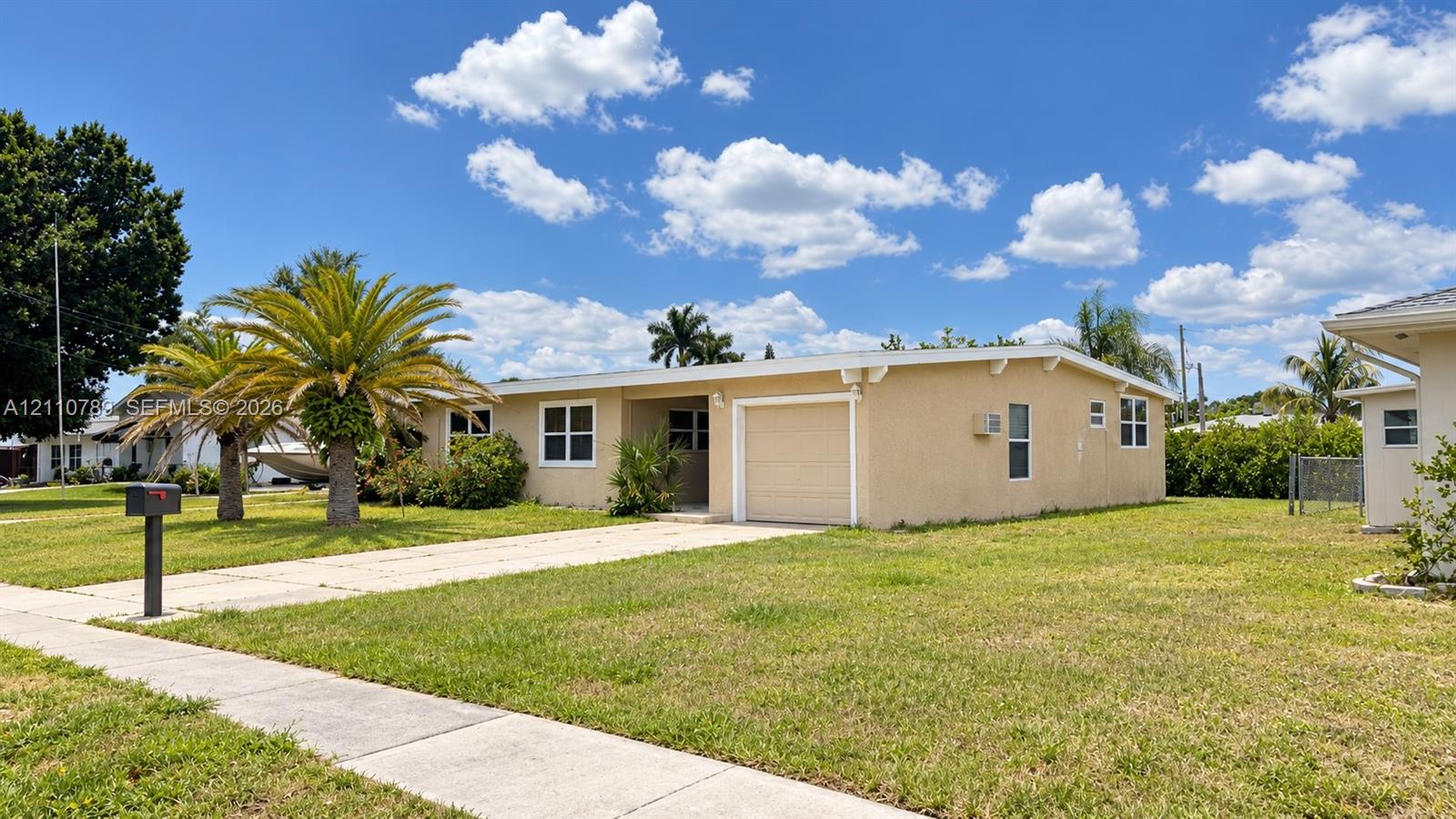 Single-story residence featuring a stucco exterior, concrete driveway, attached one-car garage, and established palm trees