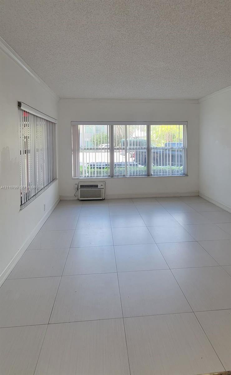 Light-filled room featuring neutral large-format tile flooring, textured ceilings, and expansive multi-pane windows with vertical blinds Light-filled room featuring neutral large-format tile flooring, textured ceilings, and expansive multi-pane windows with vertical blinds