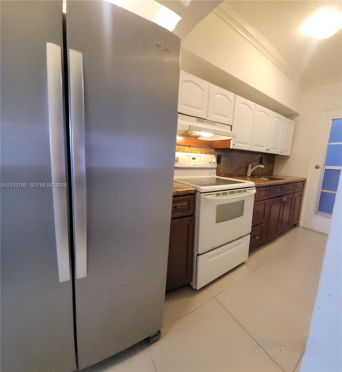 Kitchen featuring stainless steel side-by-side refrigerator, white appliance suite, dual-tone cabinetry, stone-finish countertops, and tile flooring Kitchen featuring stainless steel side-by-side refrigerator, white appliance suite, dual-tone cabinetry, stone-finish countertops, and tile flooring