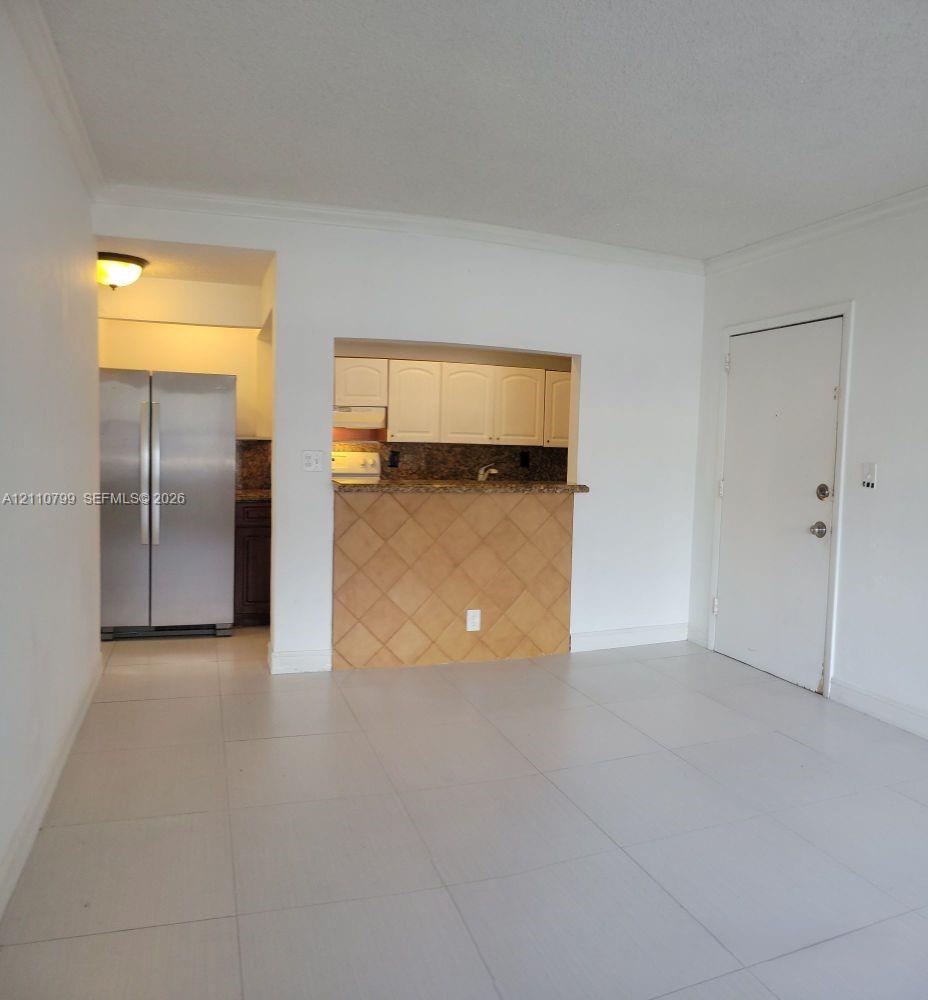 Kitchen featuring a pass-through opening, stone-finish countertops, tile-front breakfast bar, and stainless steel refrigerator, complemented by large-format floor tiling Kitchen featuring a pass-through opening, stone-finish countertops, tile-front breakfast bar, and stainless steel refrigerator, complemented by large-format floor tiling