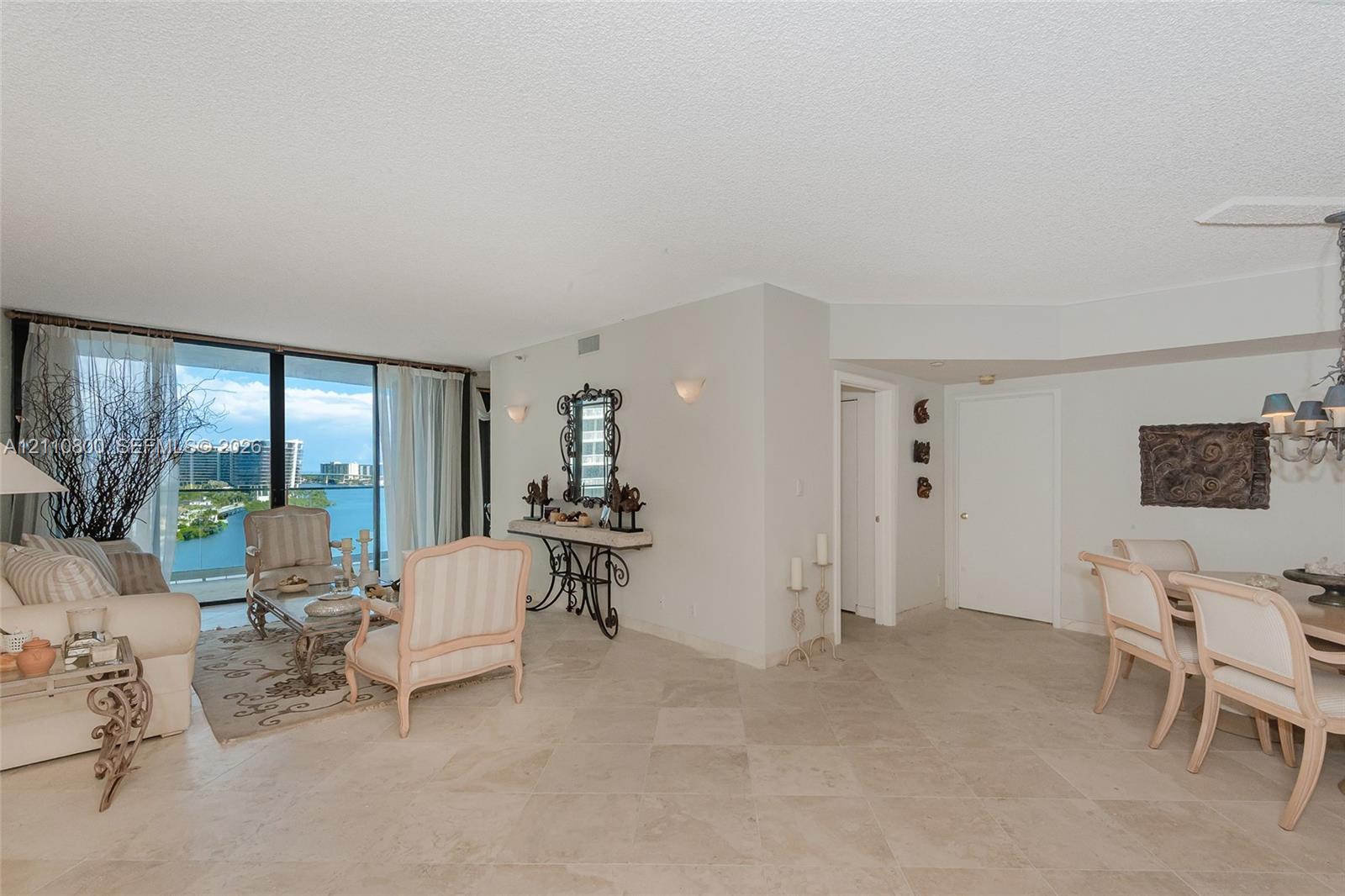 Open-concept living space featuring neutral stone-finish tile flooring, floor-to-ceiling glass sliding doors, and a multi-tiered crystal chandelier