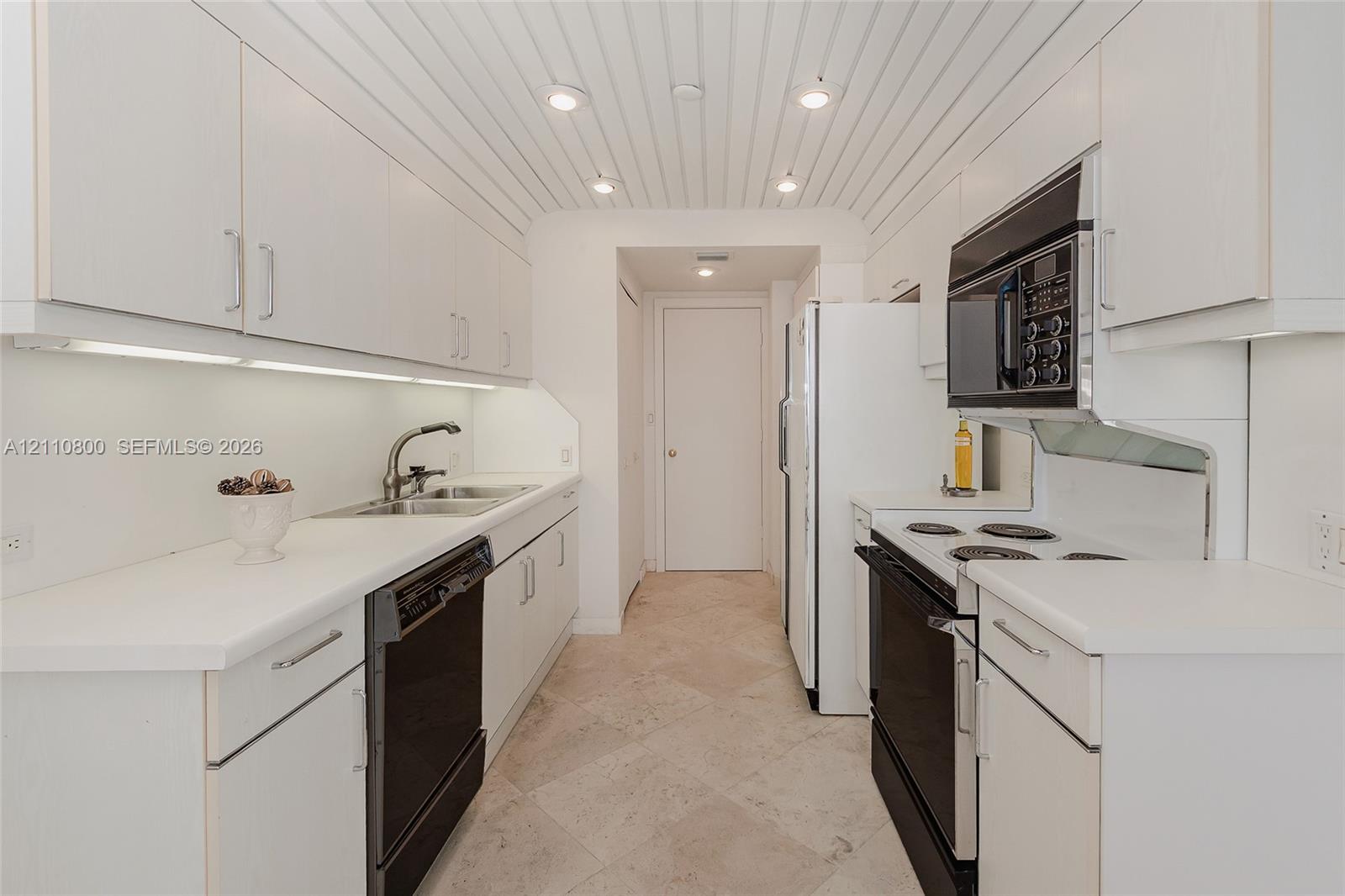 Galley kitchen featuring white cabinetry, under-cabinet lighting, a vertical-plank ceiling with recessed lighting, stone-tile flooring, and built-in appliances