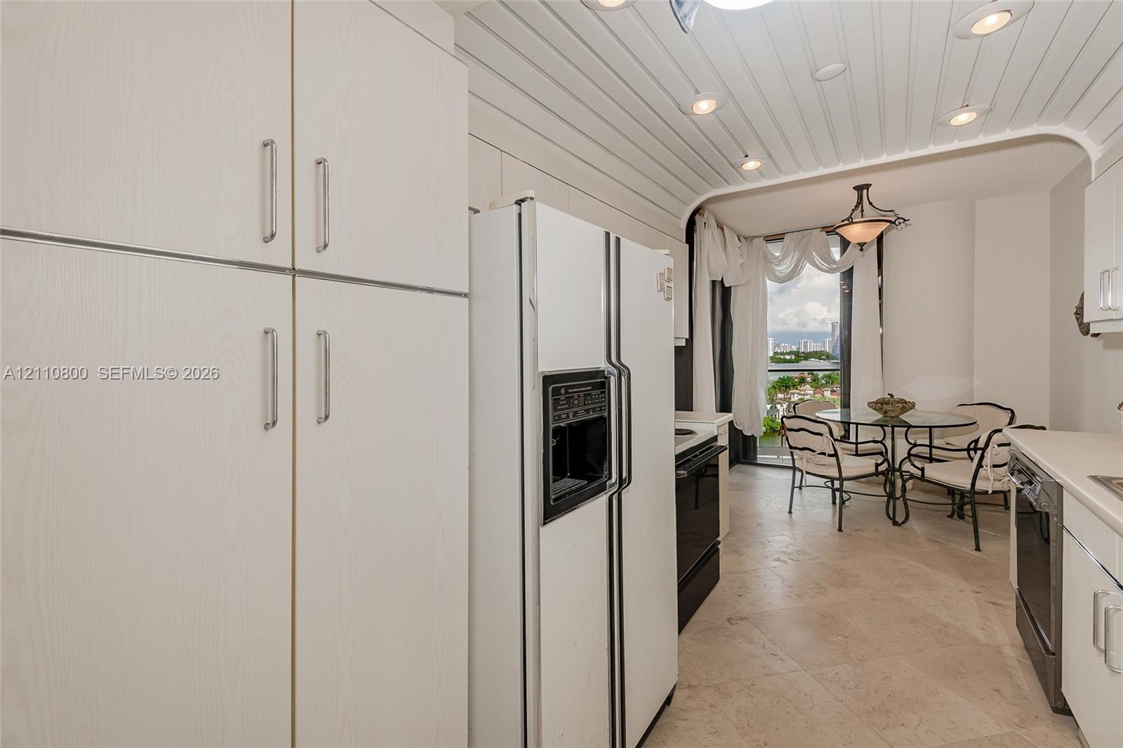 Kitchen featuring full-height cabinetry, stone tile flooring, recessed ceiling lighting, and a curved architectural ceiling detail