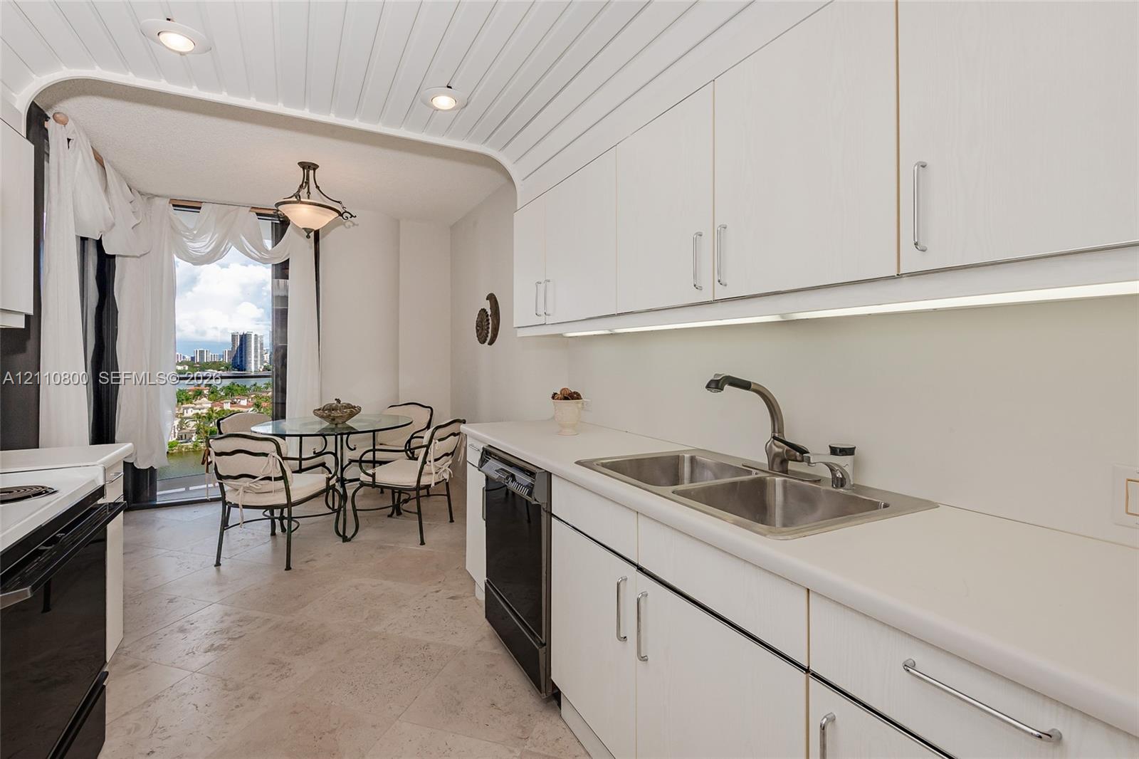 Kitchen featuring white cabinetry, solid-surface countertops, dual-basin stainless steel sink, under-cabinet lighting, and plank-style ceiling detail