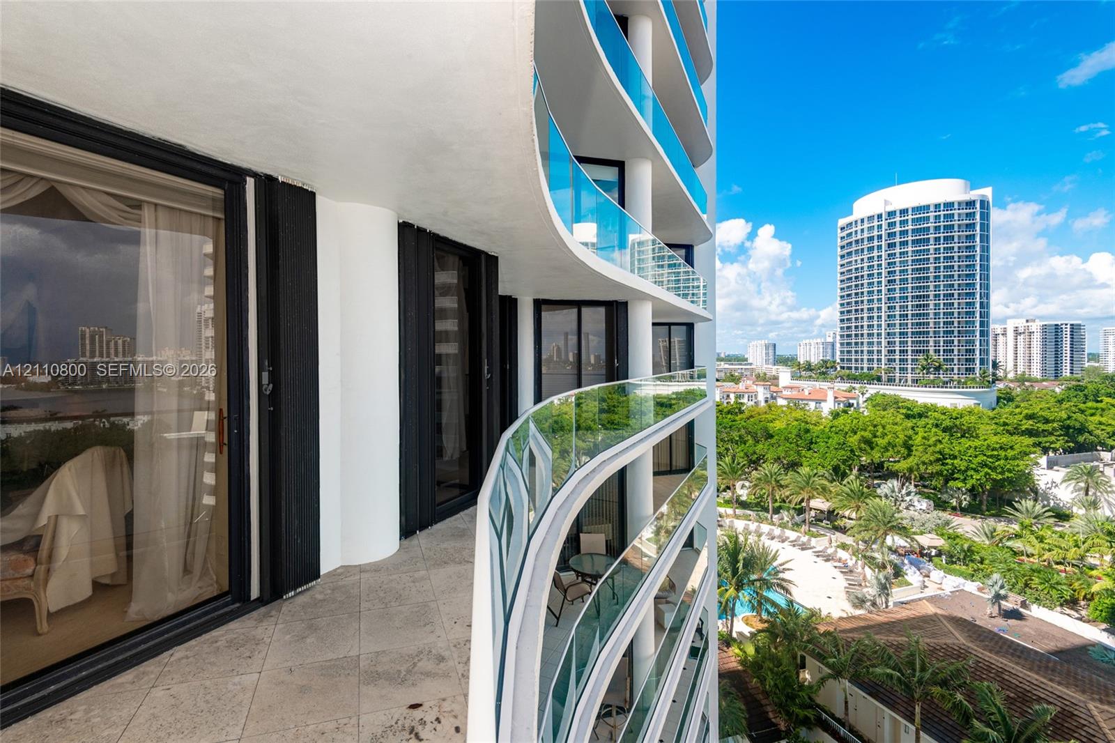 Curved private balcony with stone-tile flooring, glass panel railings, and floor-to-ceiling sliding glass doors