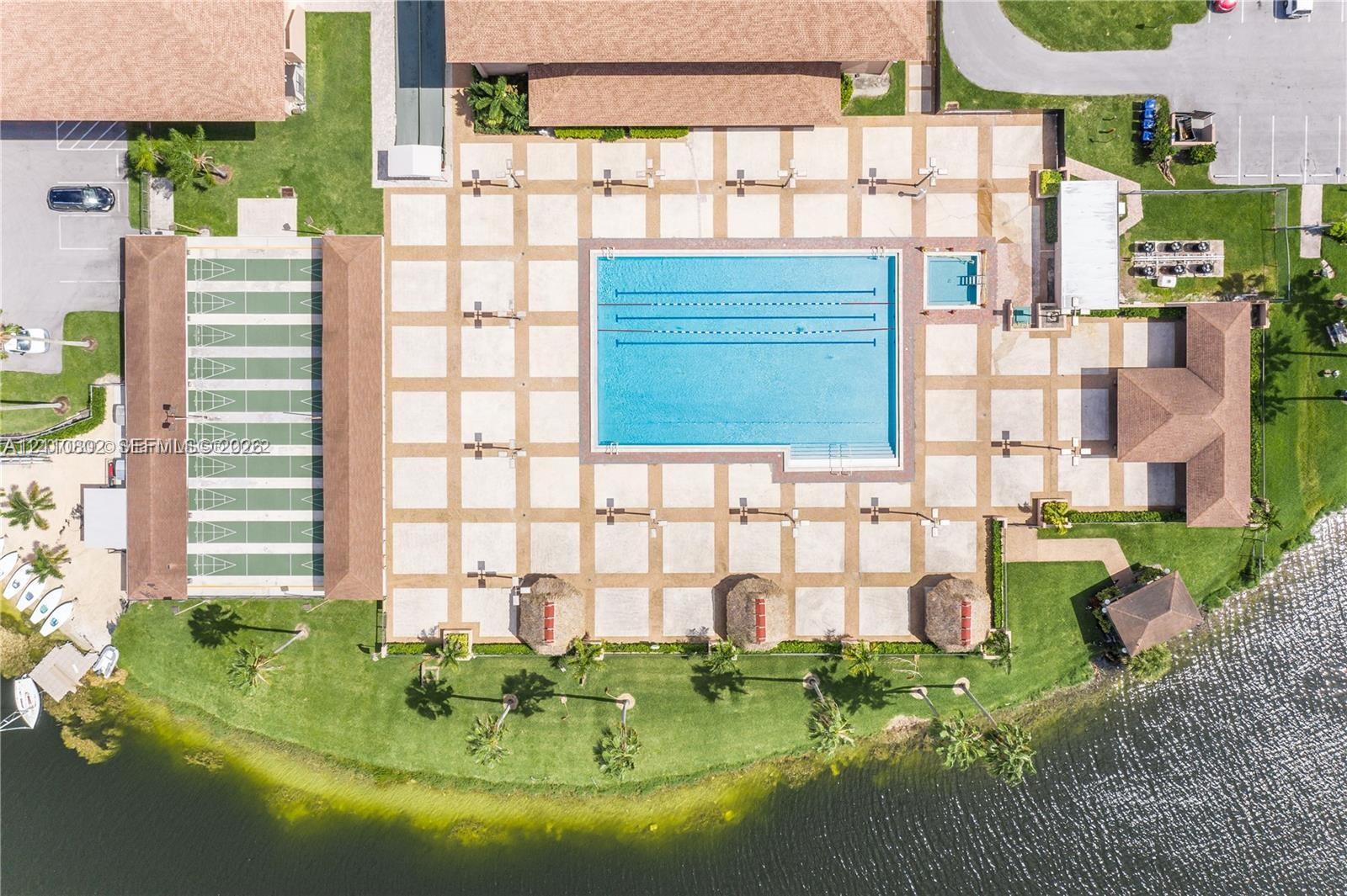Recreational area featuring a large swimming pool, shuffleboard courts, thatched-roof gazebos, and waterfront positioning