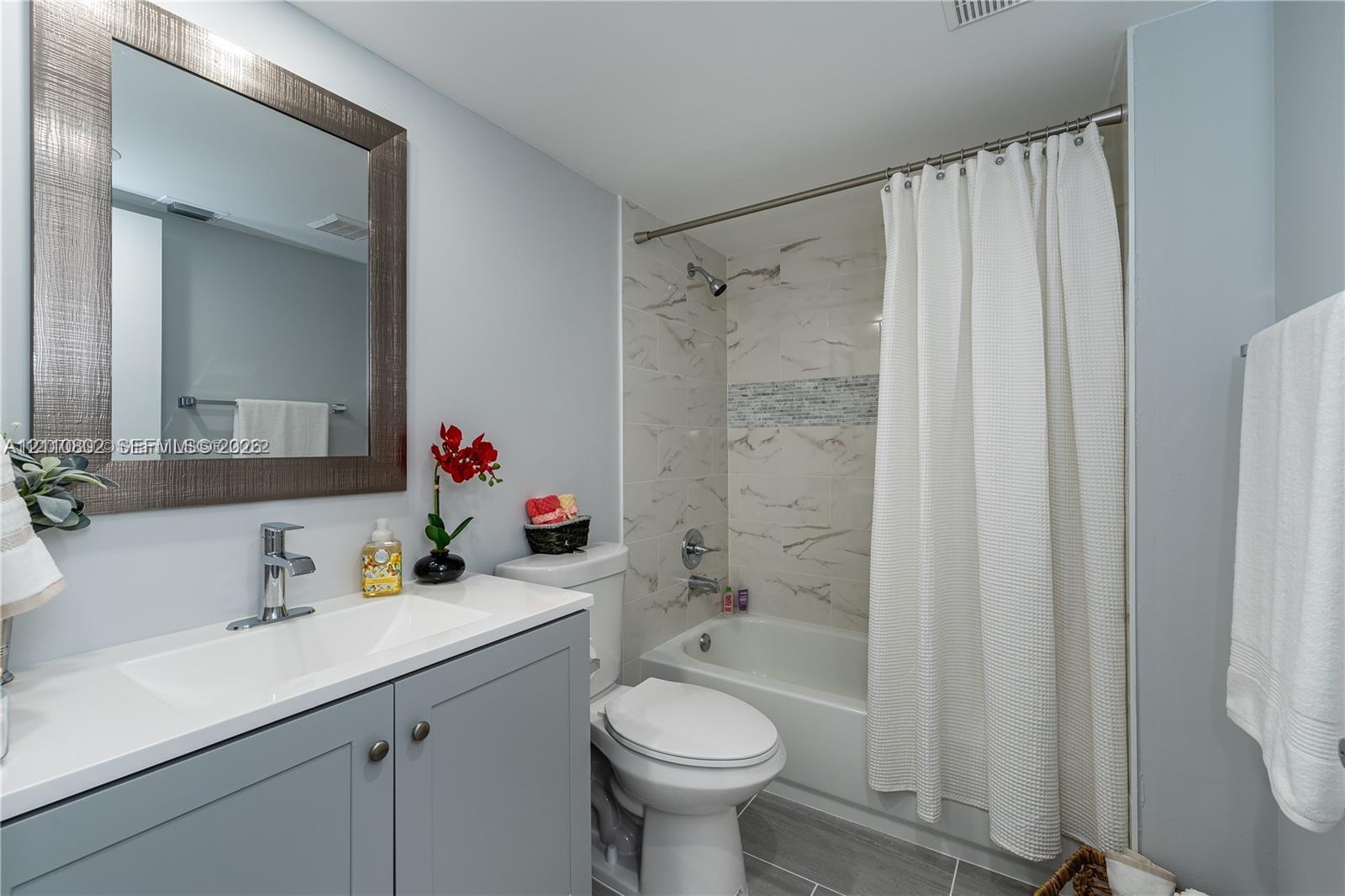 Bathroom featuring a vanity with a white countertop and integrated sink, a framed wall mirror, and a shower-tub combination with light-toned wall tile and a mosaic accent band