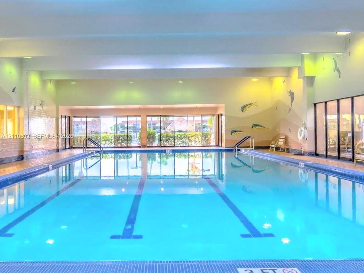 Indoor lap pool featuring tile perimeter, multi-lane markings, metal handrails, and expansive floor-to-ceiling glass windows