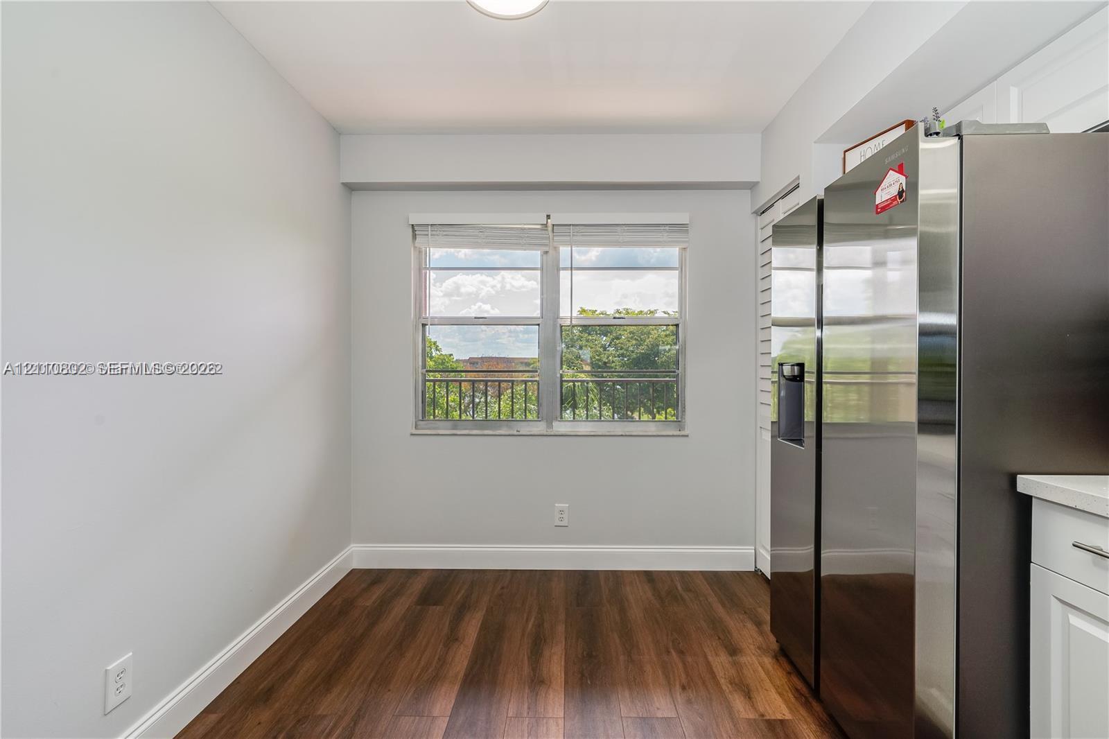Wood-finish flooring, stainless steel side-by-side refrigerator, white shaker-style cabinetry, and horizontal sliding window with metal railing Wood-finish flooring, stainless steel side-by-side refrigerator, white shaker-style cabinetry, and horizontal sliding window with metal railing