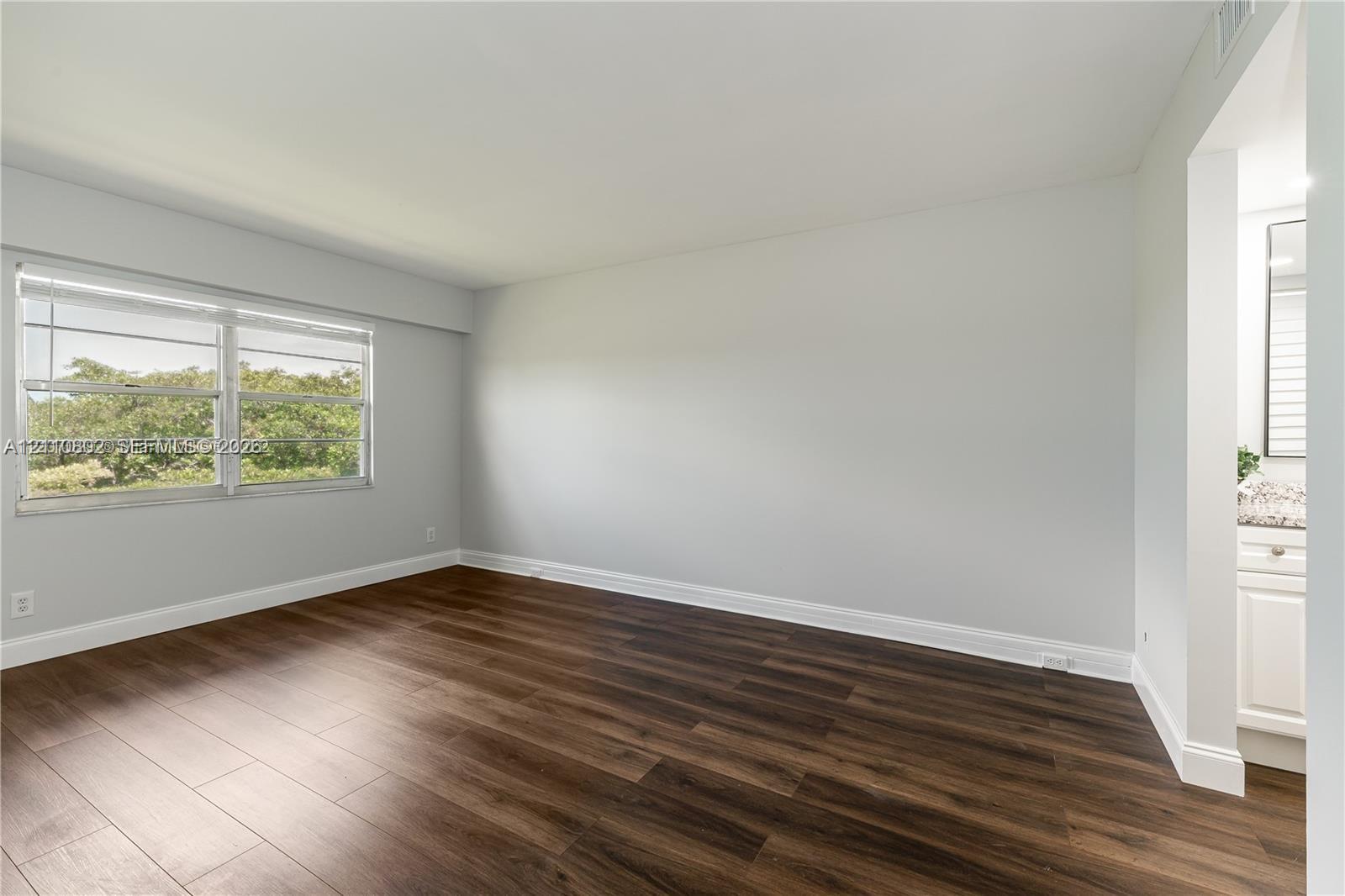 Room featuring wood-finish flooring, neutral wall paint, and a large window with greenery backdrop