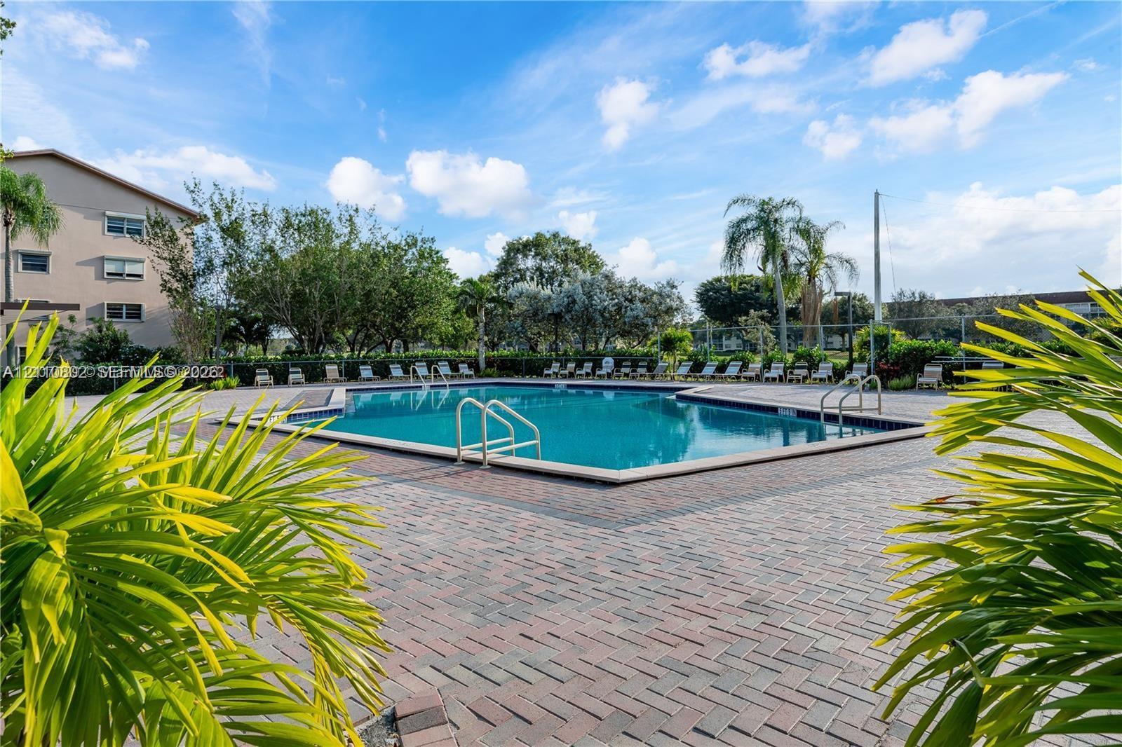 Outdoor swimming pool featuring a brick-paver deck, metal safety railings, and surrounding tropical landscaping