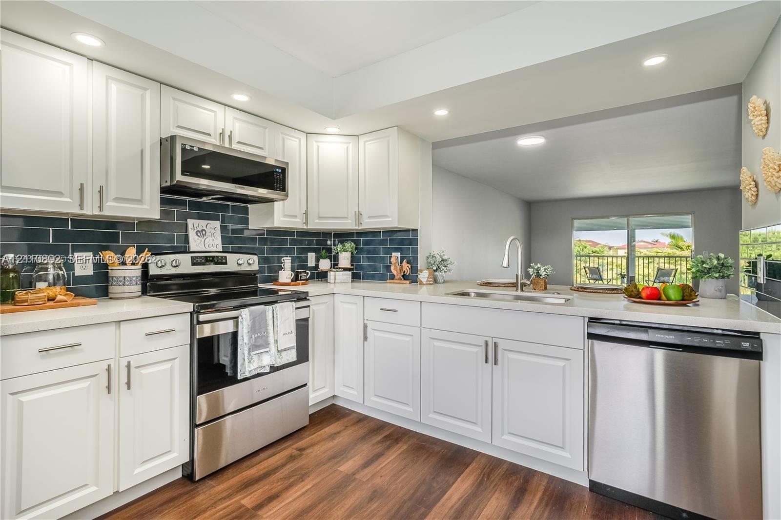 Kitchen featuring white cabinetry, stainless steel appliances, dark tile backsplash, light-toned countertops, and wood-finish flooring Kitchen featuring white cabinetry, stainless steel appliances, dark tile backsplash, light-toned countertops, and wood-finish flooring