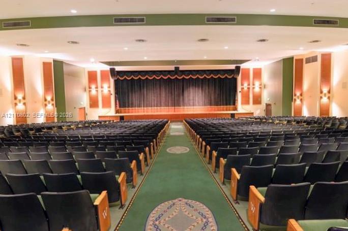 Spacious auditorium featuring tiered fixed theater-style seating, a raised stage with proscenium arch, decorative wood-paneled wall accents, and recessed ceiling lighting