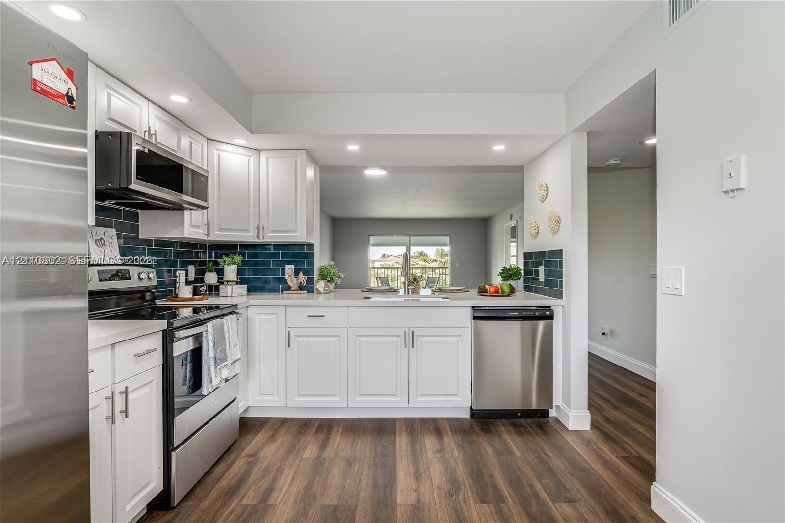 Kitchen featuring white shaker-style cabinetry, stainless steel appliances, dark subway tile backsplash, light-toned countertops, and wood-finish flooring Kitchen featuring white shaker-style cabinetry, stainless steel appliances, dark subway tile backsplash, light-toned countertops, and wood-finish flooring